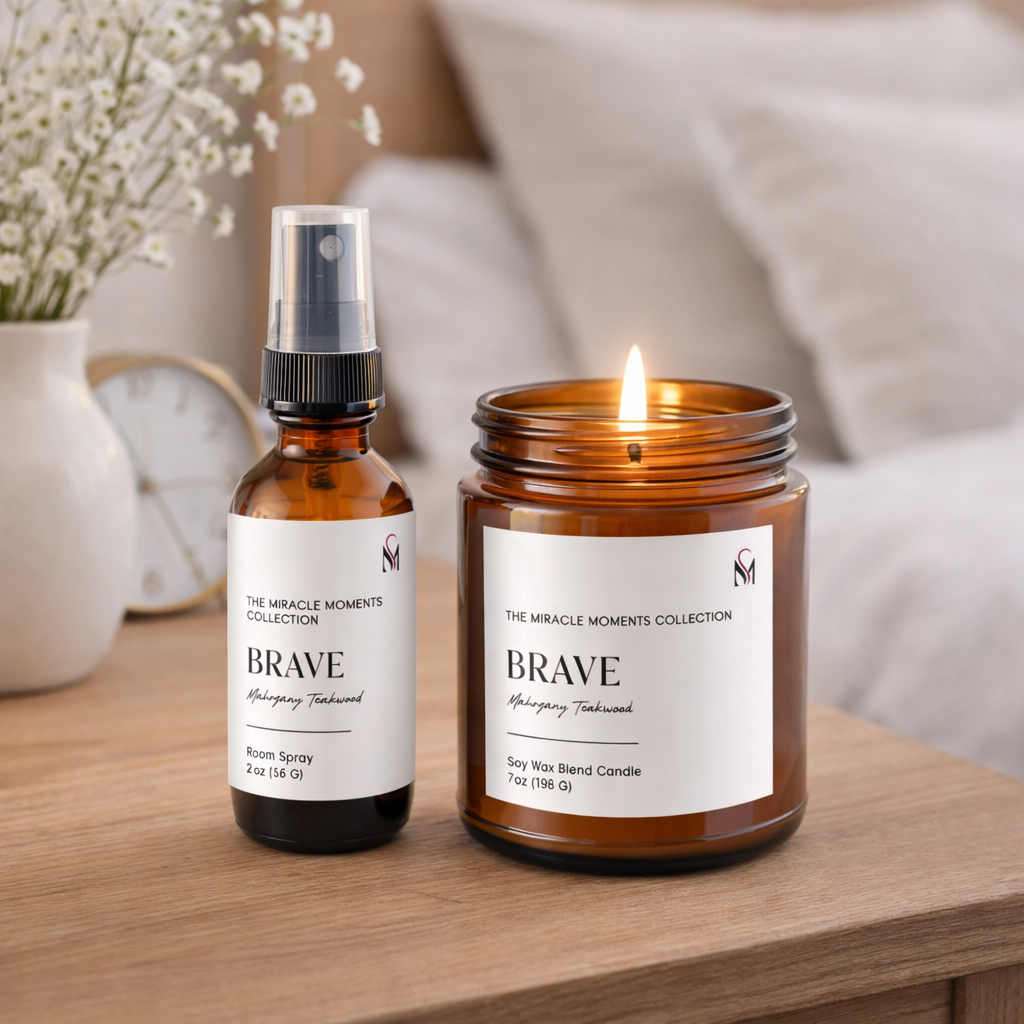 A room with a candle and a spray bottle on a wooden surface. The candle is lit, and both items have labels from the Miracle Moments Collection by Mahogany Teakwood. A vase with small white flowers and a clock are in the background.