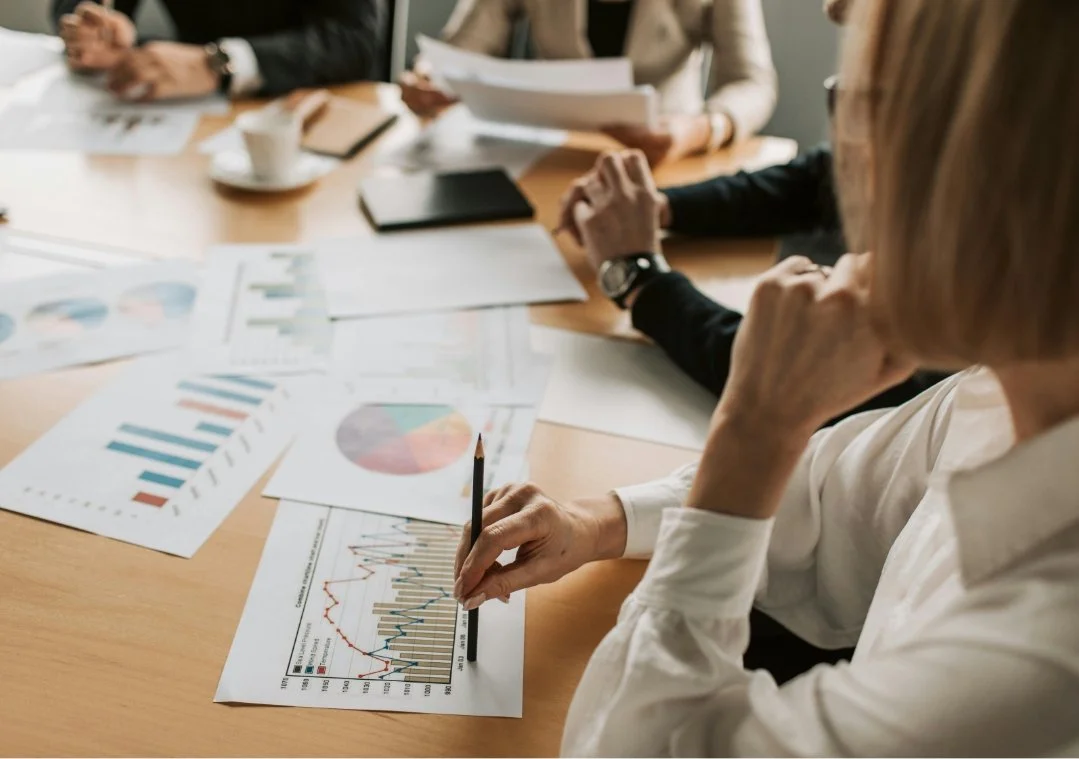 Business meeting with people analyzing charts and graphs on documents at a conference table.