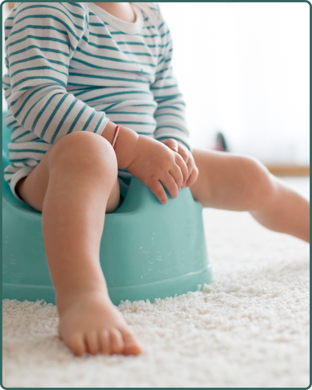A young child sitting on a potty chair, wearing a striped long-sleeve shirt and a red bracelet, with a fluffy white carpet underneath.