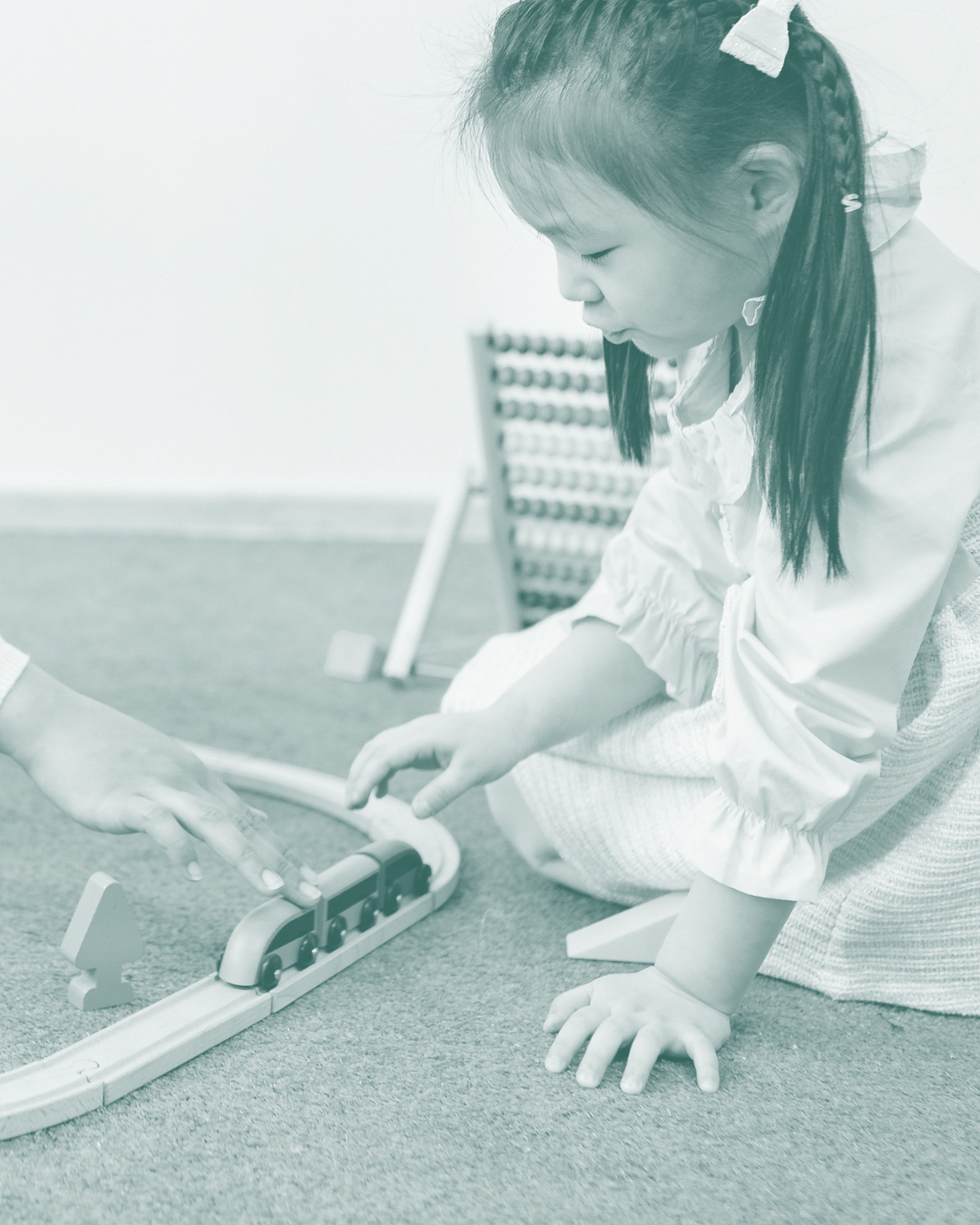 Child and adult playing with a wooden toy train on a track on the floor.
