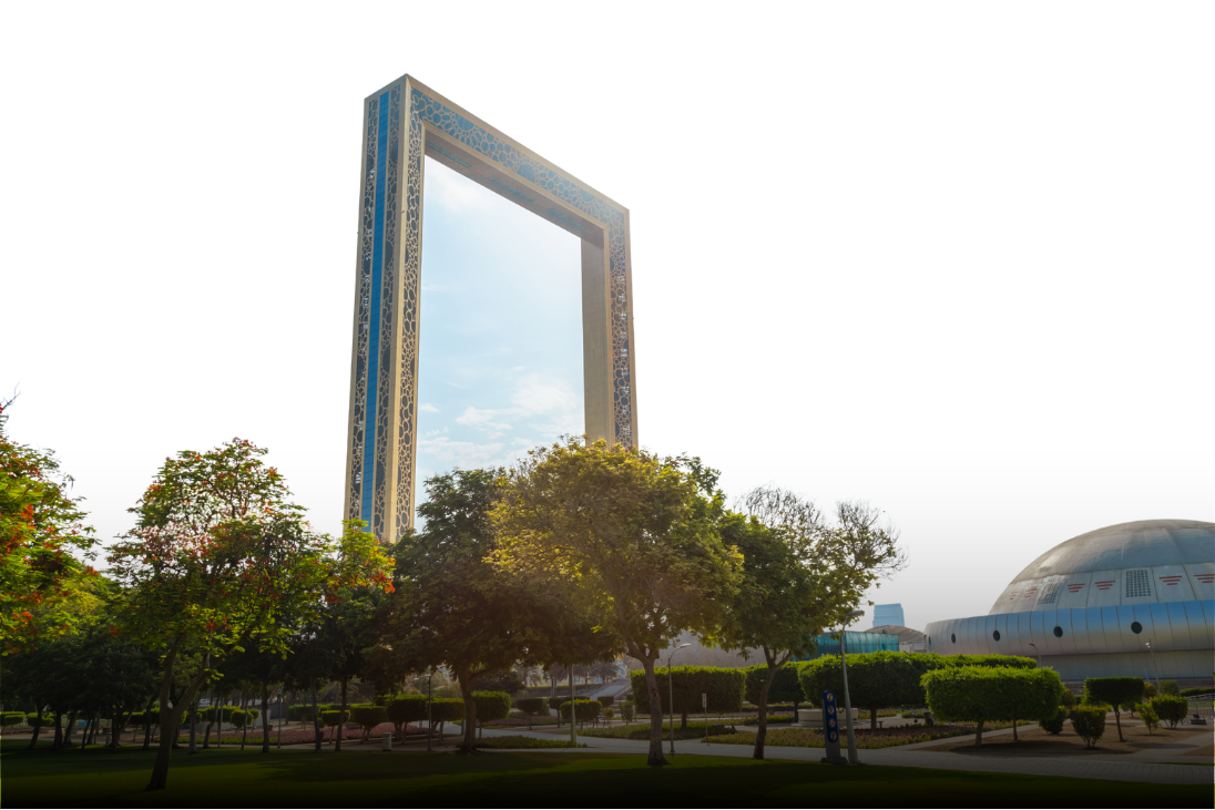 The Dubai Frame, a large rectangular arch structure, standing tall against a partly cloudy sky, surrounded by trees and a nearby domed building.