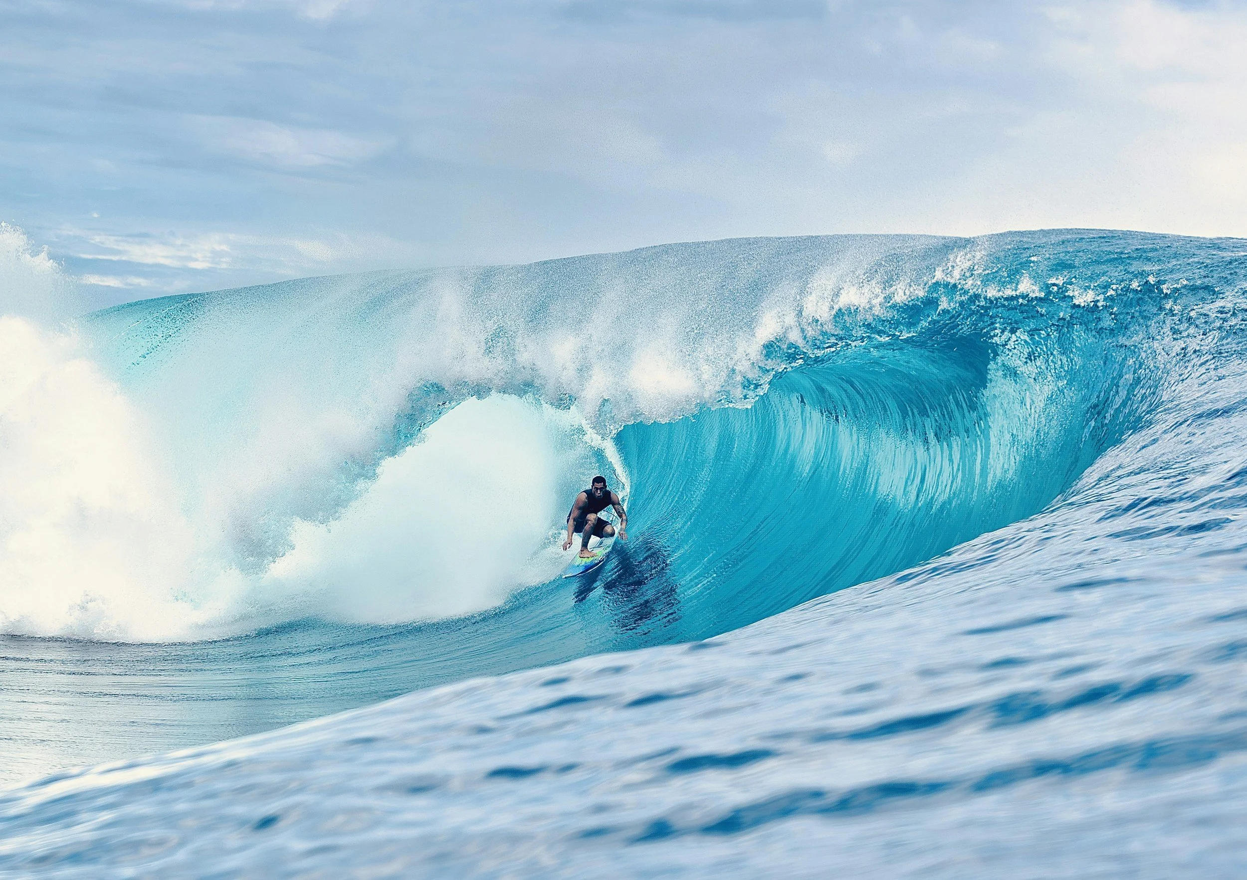 A person surfing on a large blue ocean wave.