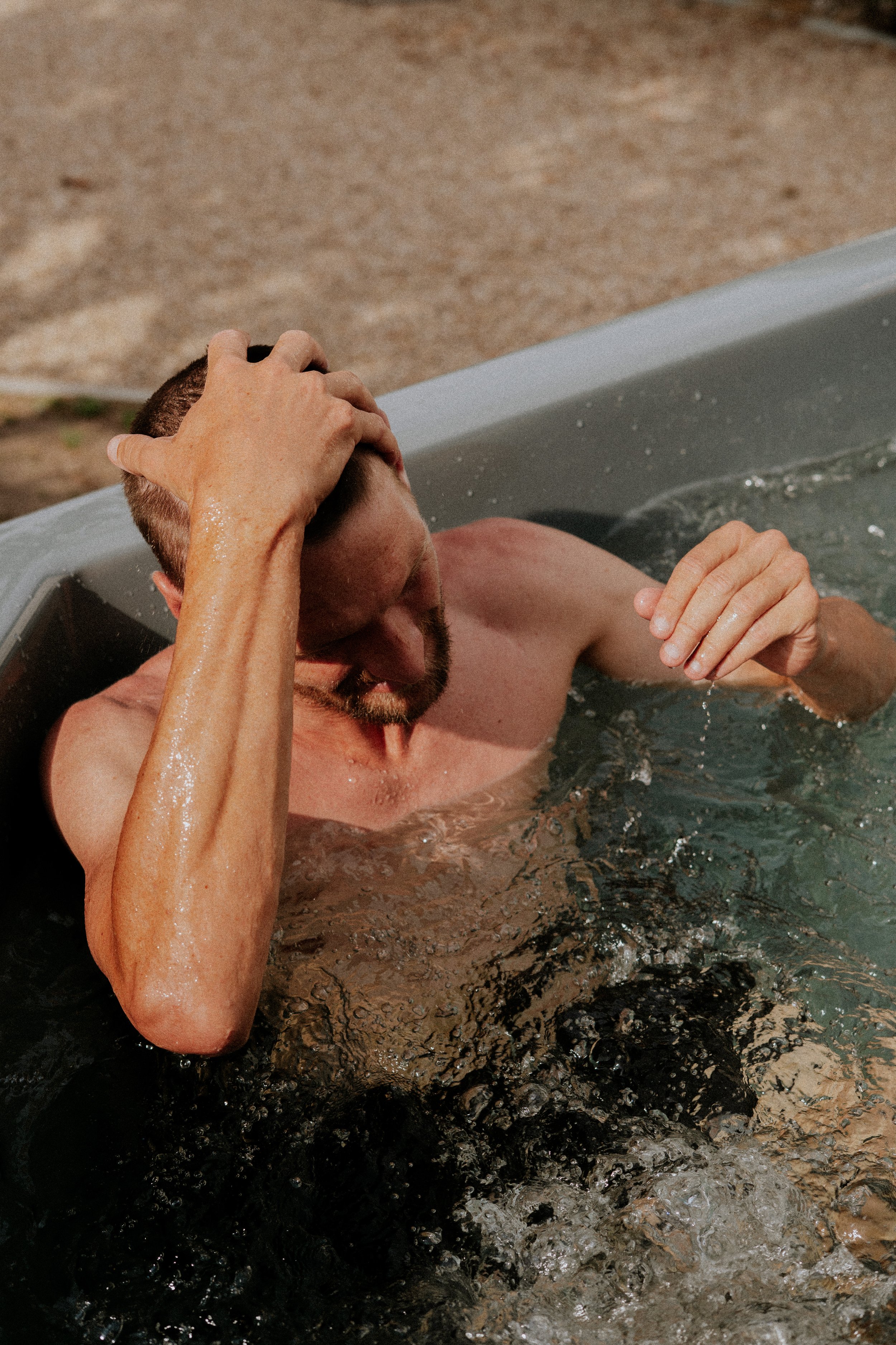 Une personne détend dans une baignoire d'eau tiède ou chaude, avec ses mains sur sa tête et son visage partiellement immergé, dans un cadre probablement intérieur.
