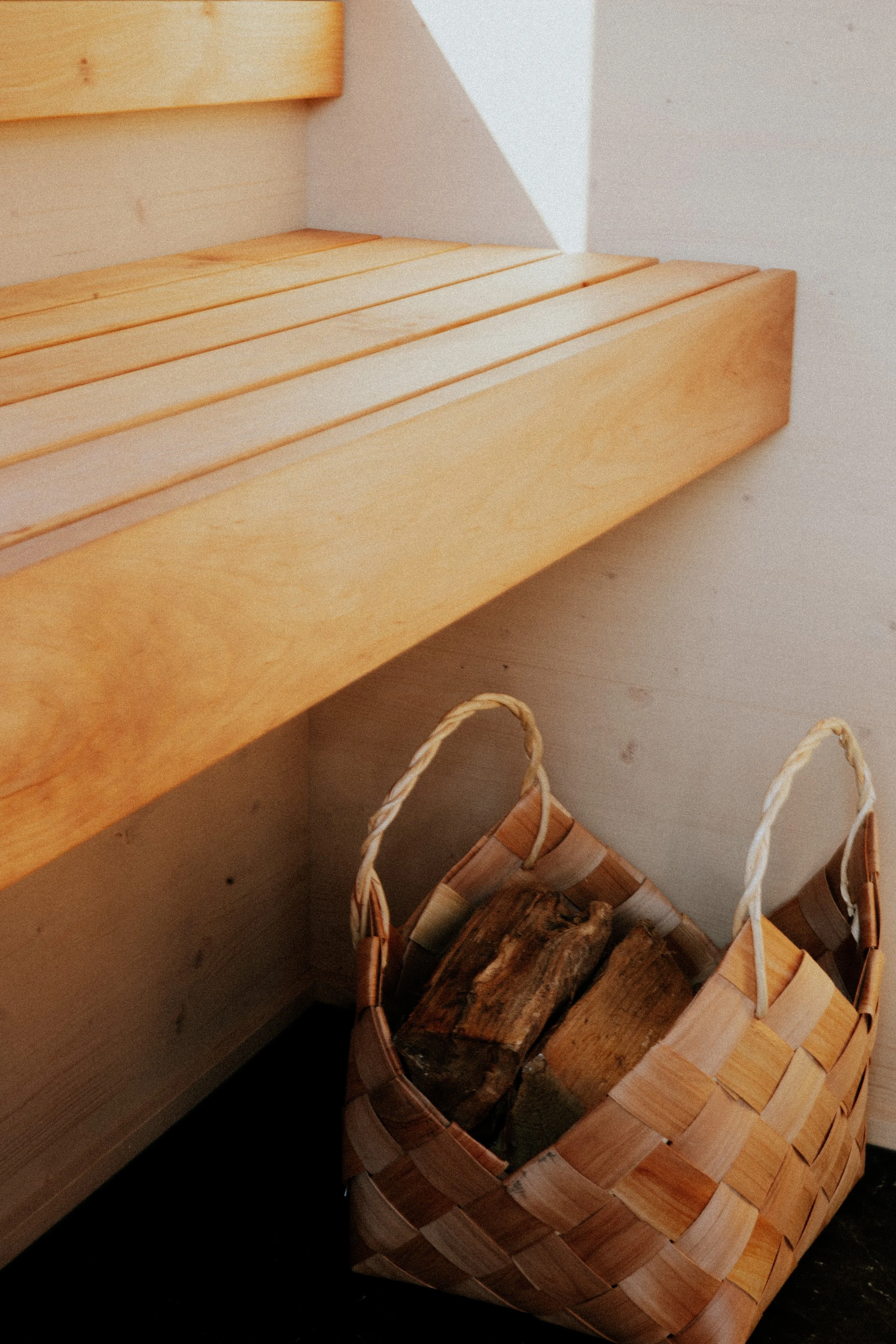 Un panier en osier rempli de morceaux de bois, posé à côté d'une surface en bois clair.