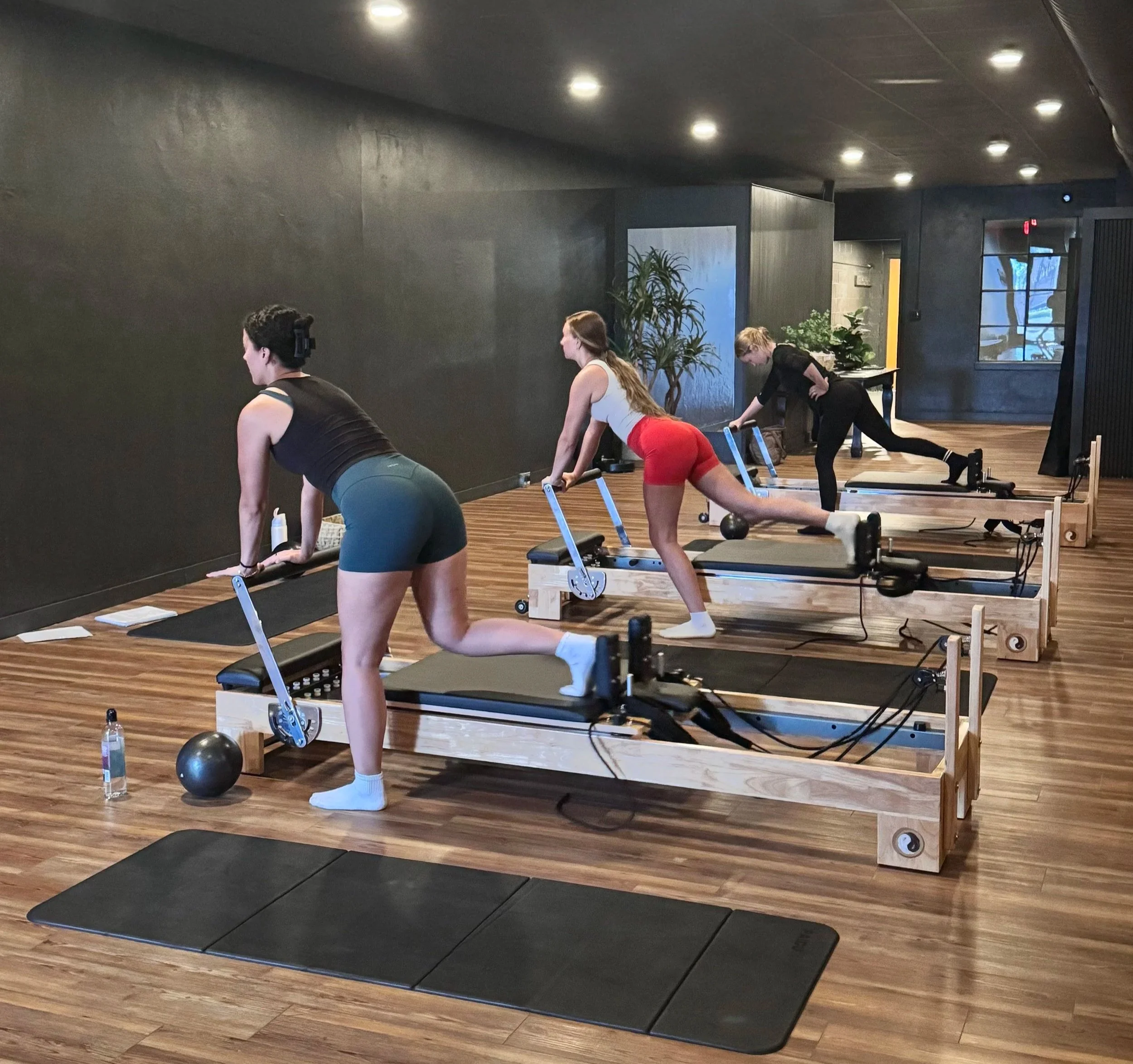 People participating in a fitness class in a gym, performing various exercises on mats and equipment.