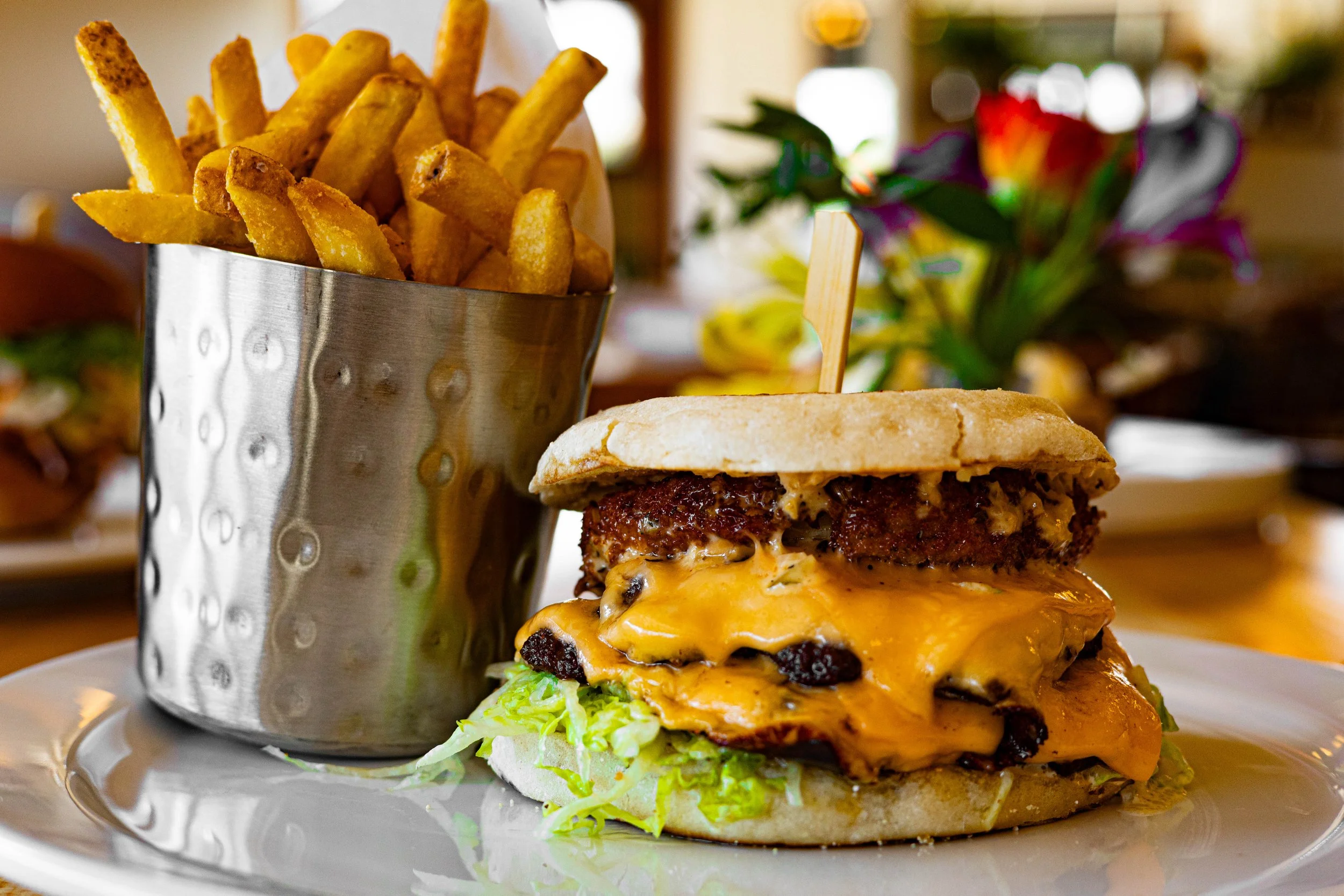 A cheeseburger with lettuce, melted cheddar, and a beef patty on a bun, served with a side of French fries in a metal container.