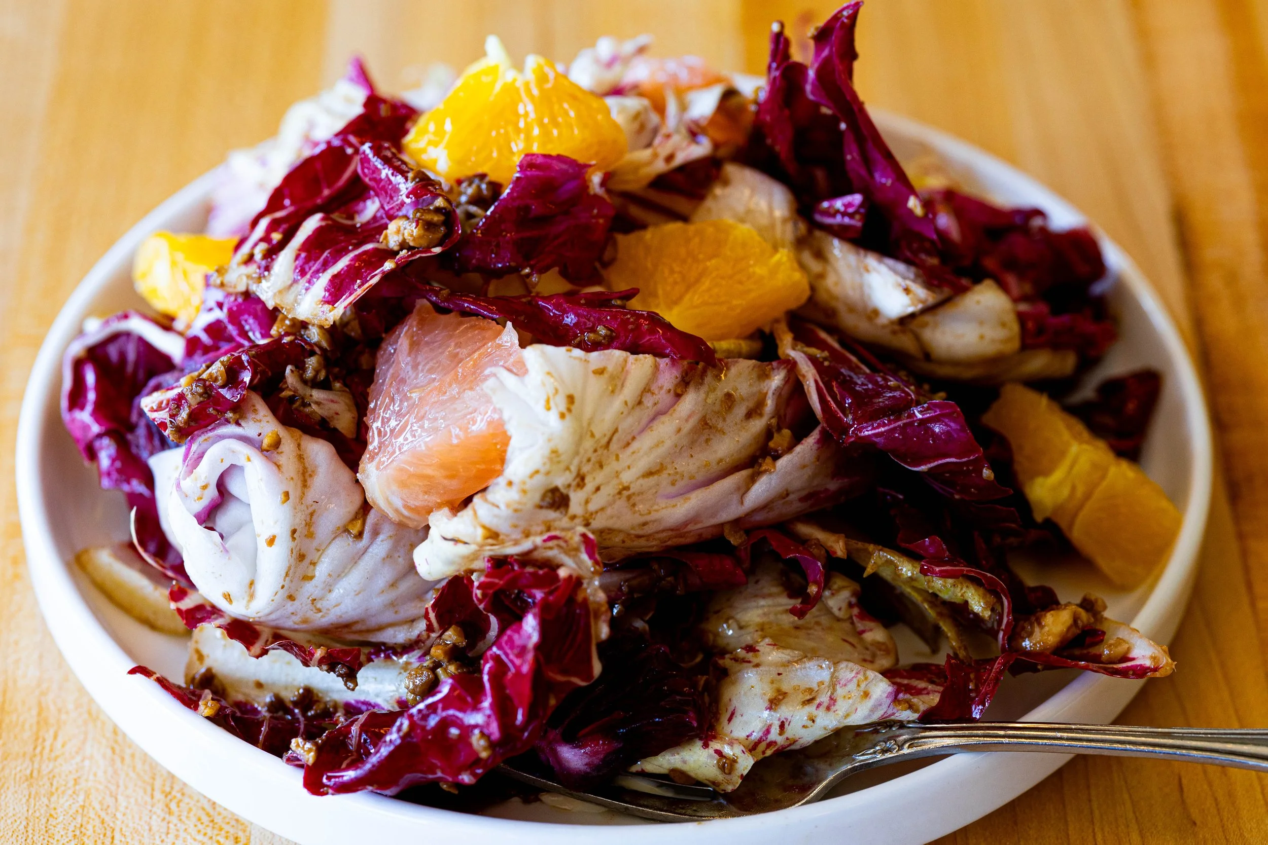 A bowl of salad with leafy greens, mandarin orange segments, and grapefruit pieces, served on a wooden surface.