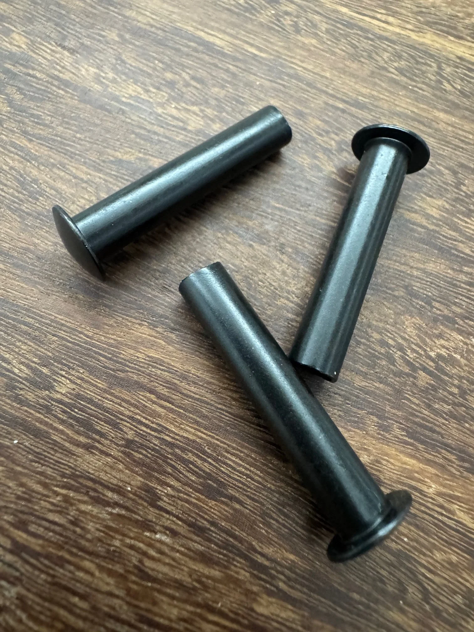 Three black metal pins with round flat heads on a wooden surface.