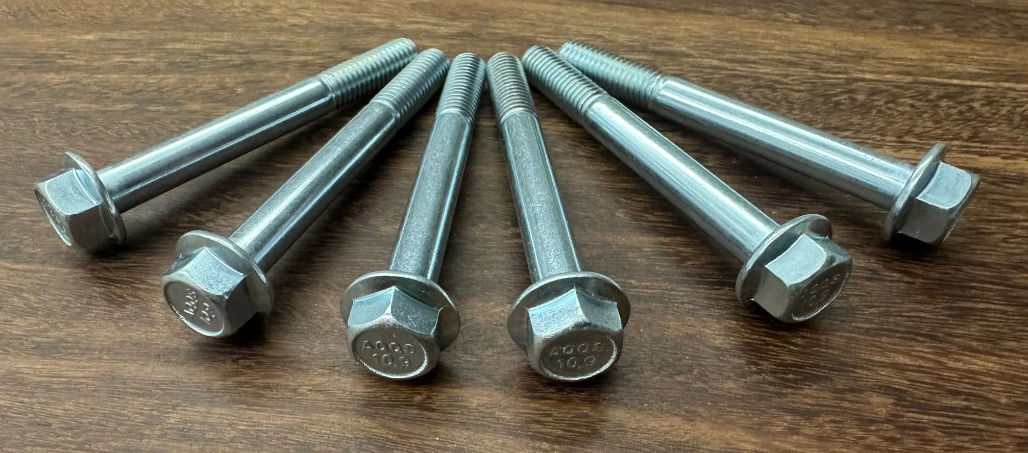 Six shiny metal bolts with hexagonal heads placed on a wooden surface.