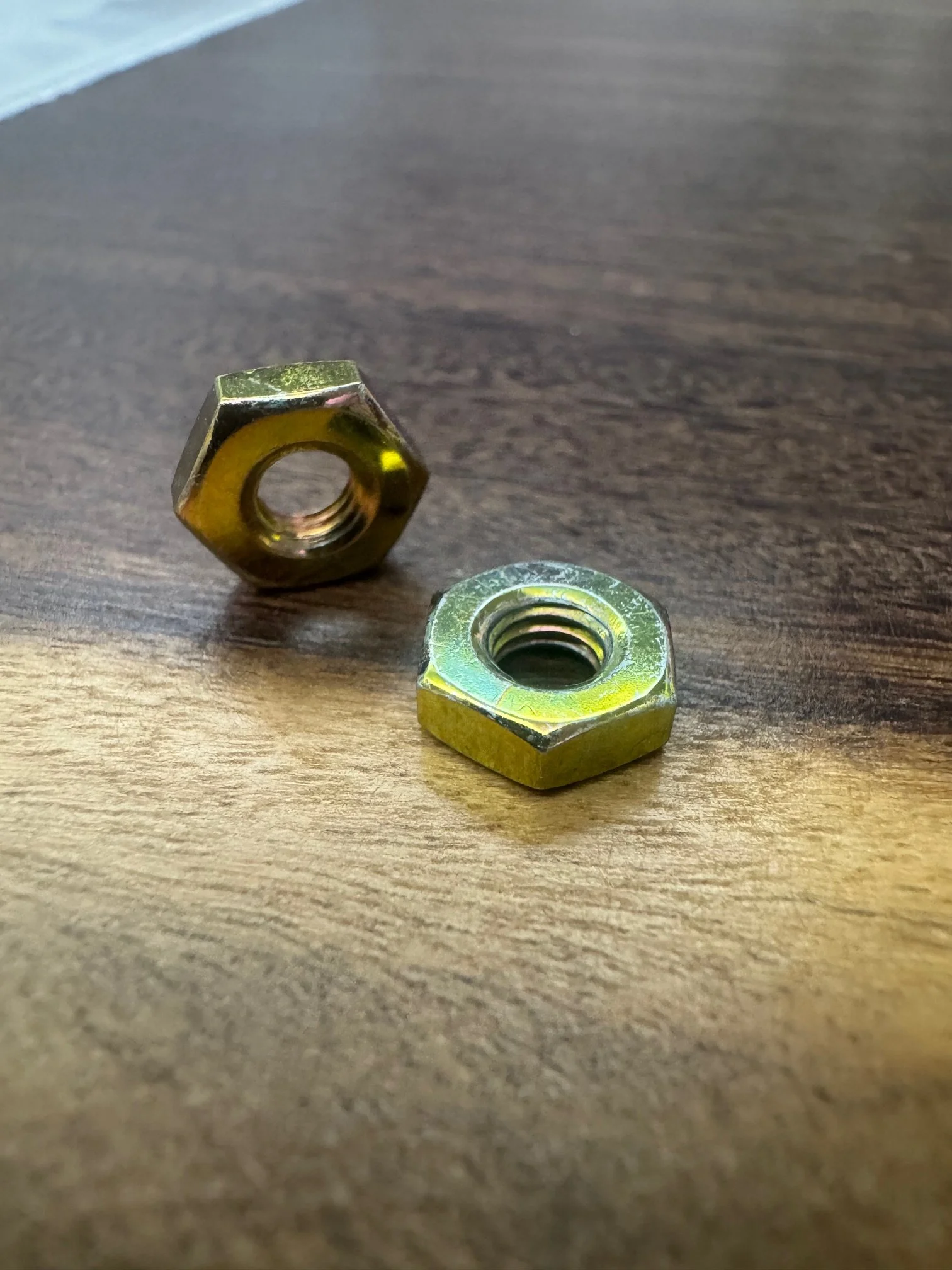 Two metal nuts on a wooden surface, one standing upright and the other lying flat.