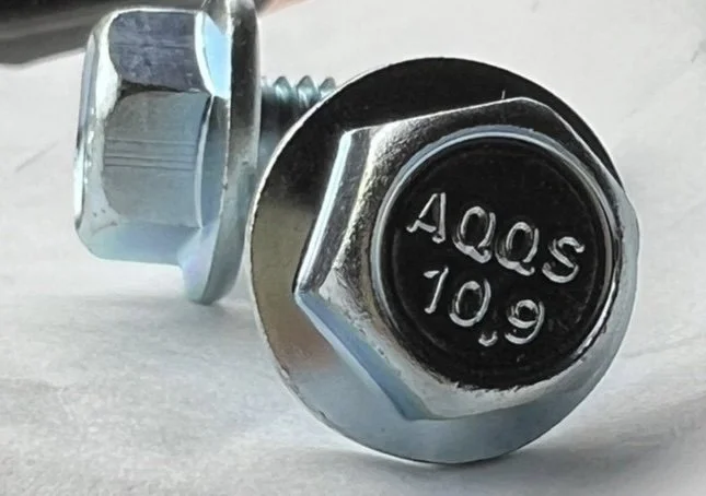 Close-up of a metallic bolt with a black head, inscribed with '50QC 10.9', on a gray surface.