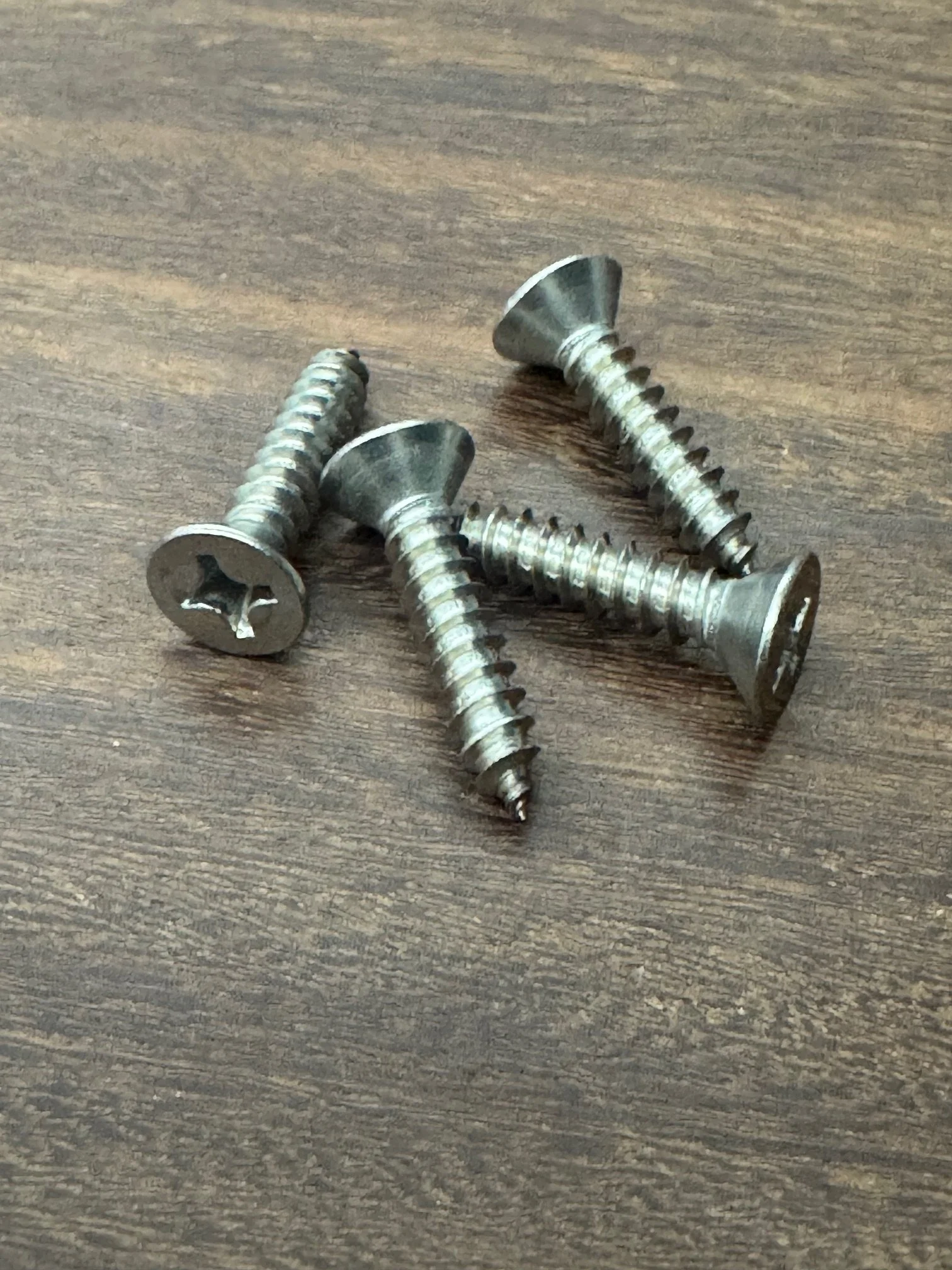 Four metal screws with Phillips heads on a wooden surface.