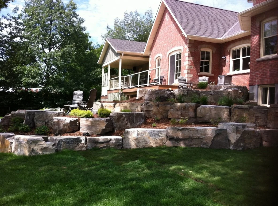 Settling the tall house into the landscape with layers of armourstone, steps and softened with plantings