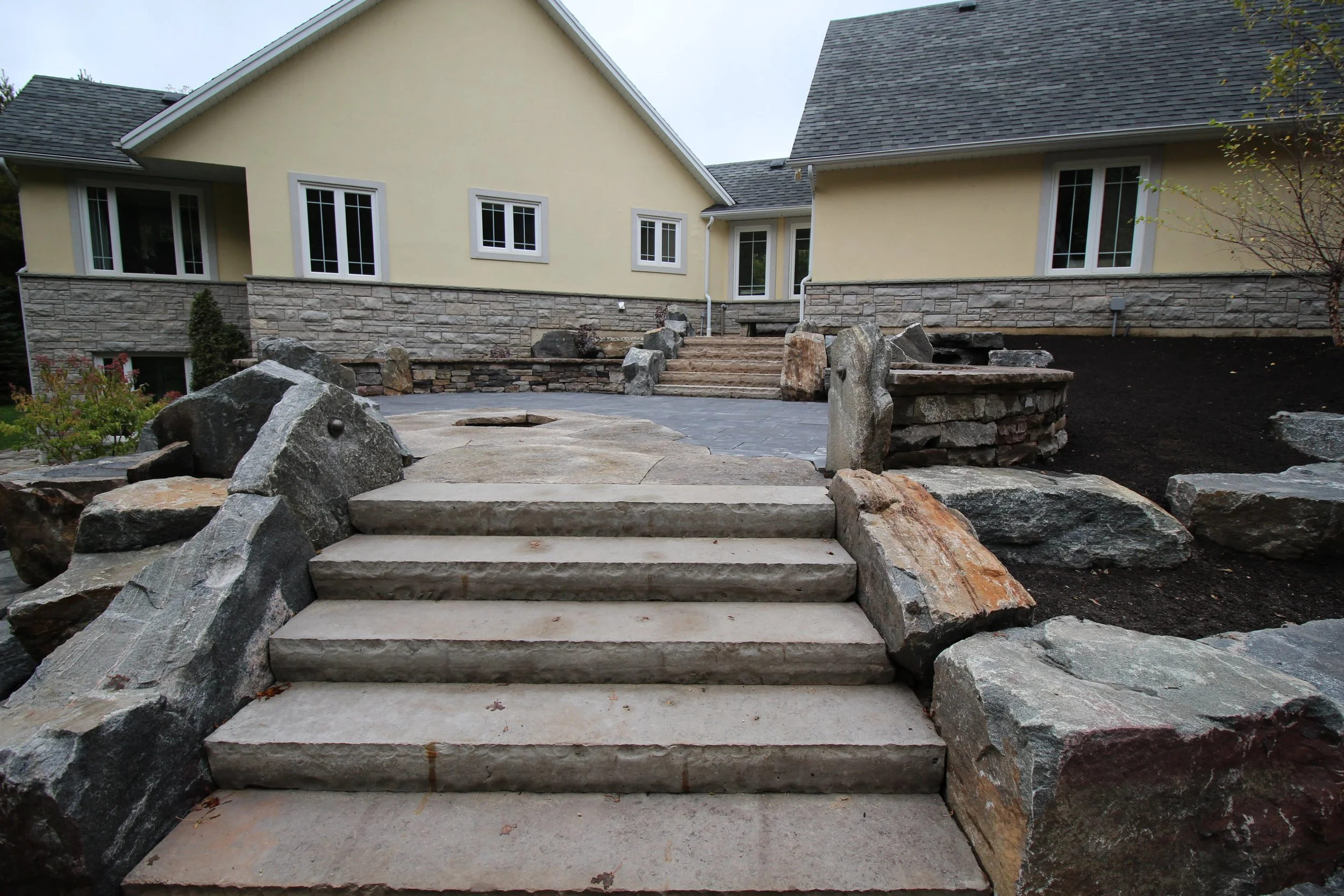 Square cut steps surrounded with granite armourstone chunks leading up to the firepit patio. 