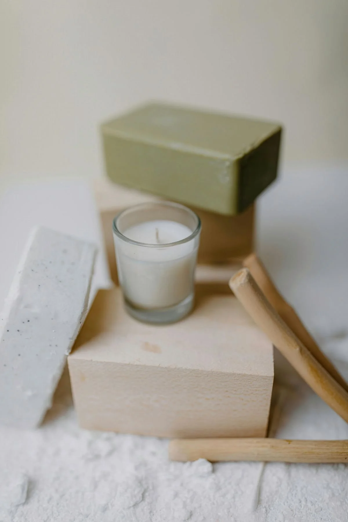 A composition of candles and wooden blocks, including a white candle in a glass holder, with blocks and wooden tools arranged around it, on a white surface.