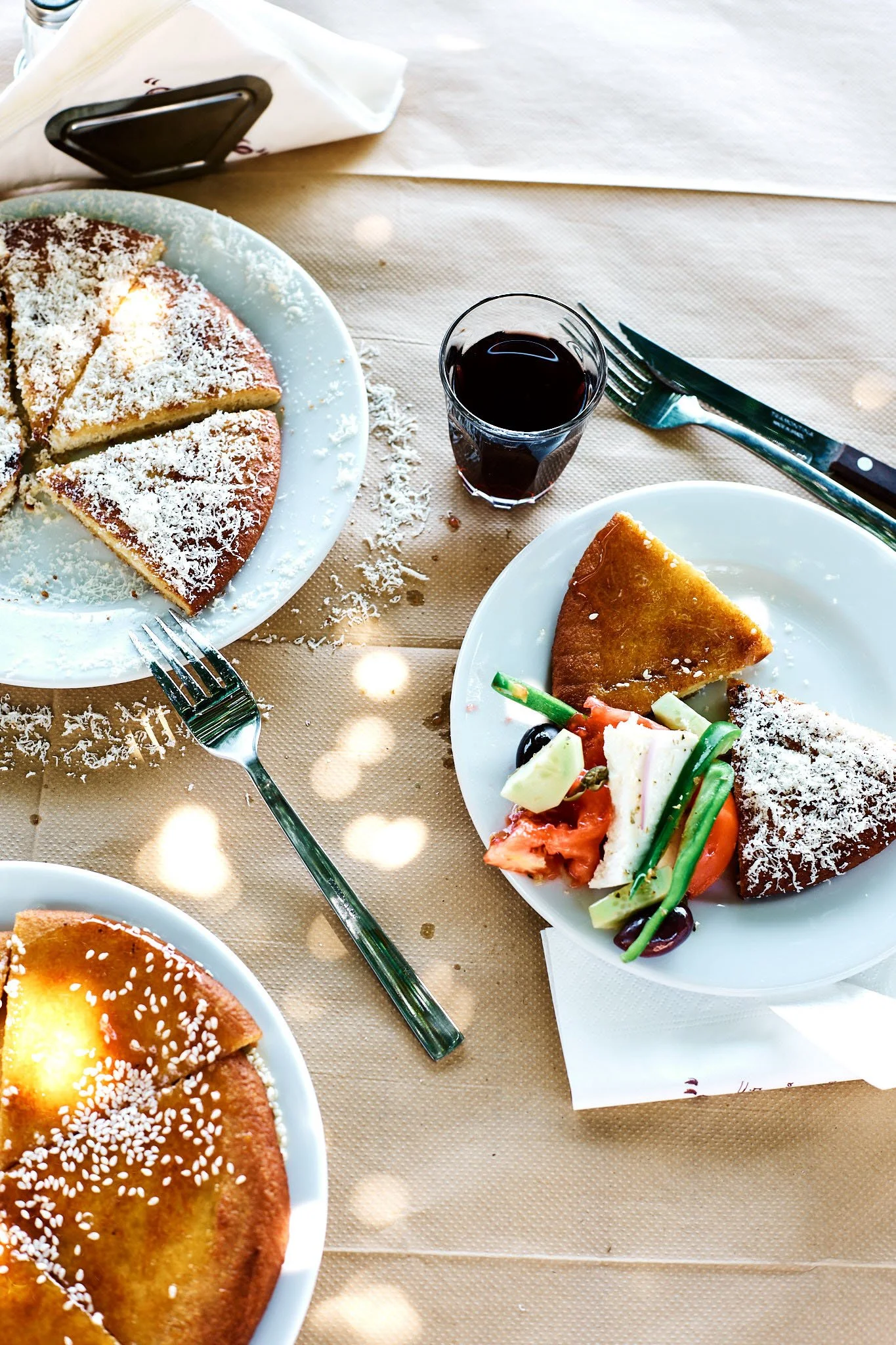 Table with plates of dessert and salad, glass of red wine, silverware, and napkin on a beige tablecloth.