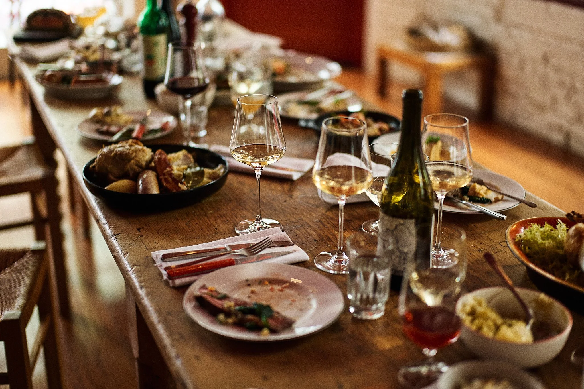 A wooden dining table with used plates, glasses of wine, and partially eaten food, indicating a meal has recently concluded.