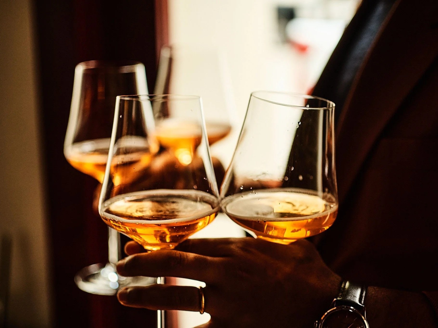 A person holding three wine glasses filled with rosé wine in a dimly lit setting.