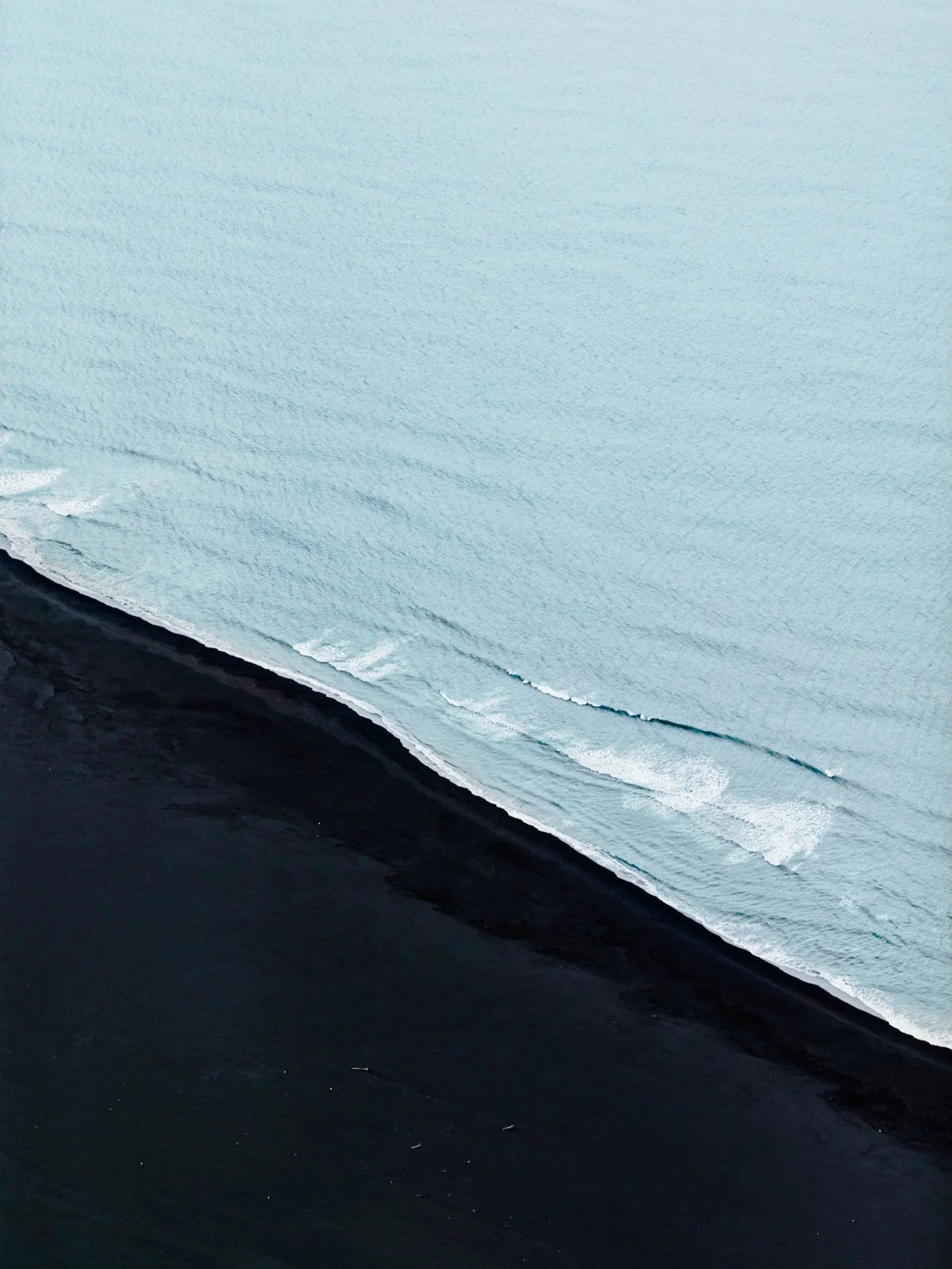 Aerial view of a coastline with black sand beach and light blue ocean waves