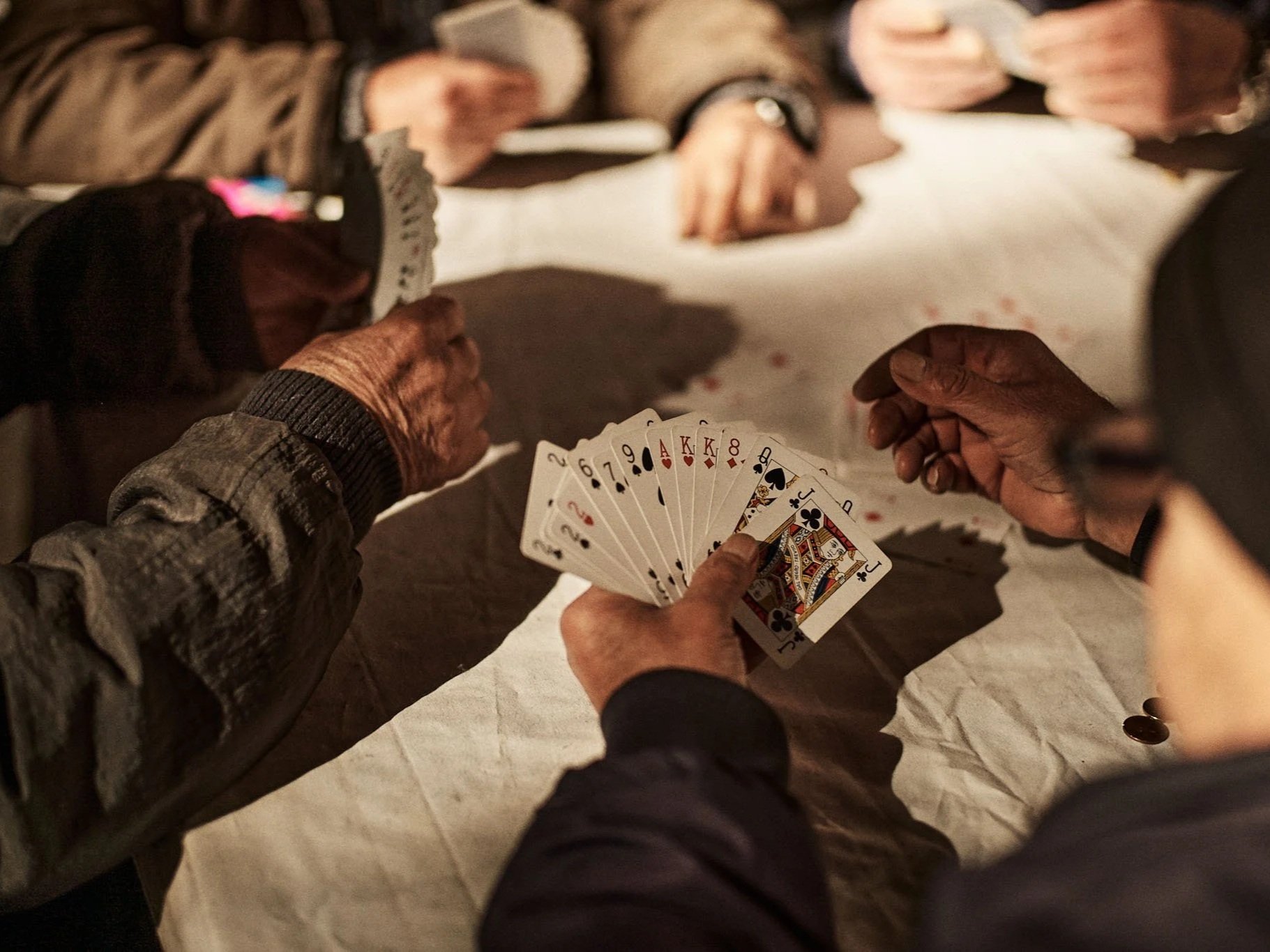 People playing cards at a table, with one person showing a hand of various playing cards including the ace of hearts and king of spades.