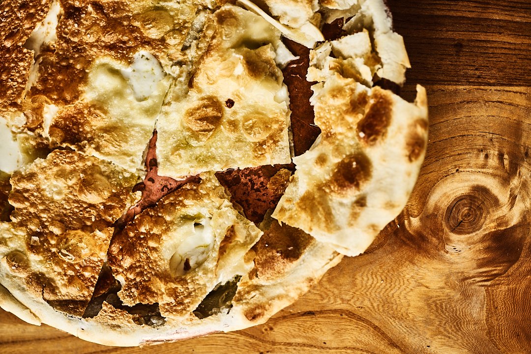 A close-up of a piece of white pizza with cheese and possibly other toppings, on a wooden surface.