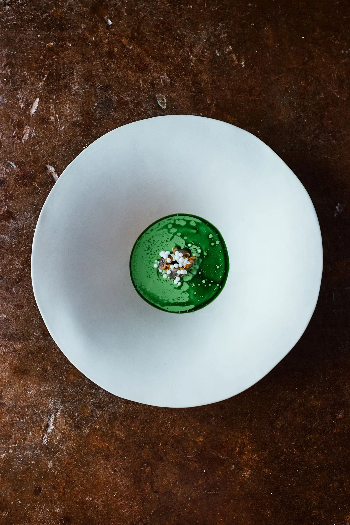 A dessert on a white plate with a green glazed top and sprinkles on top, set on a rustic brown surface.