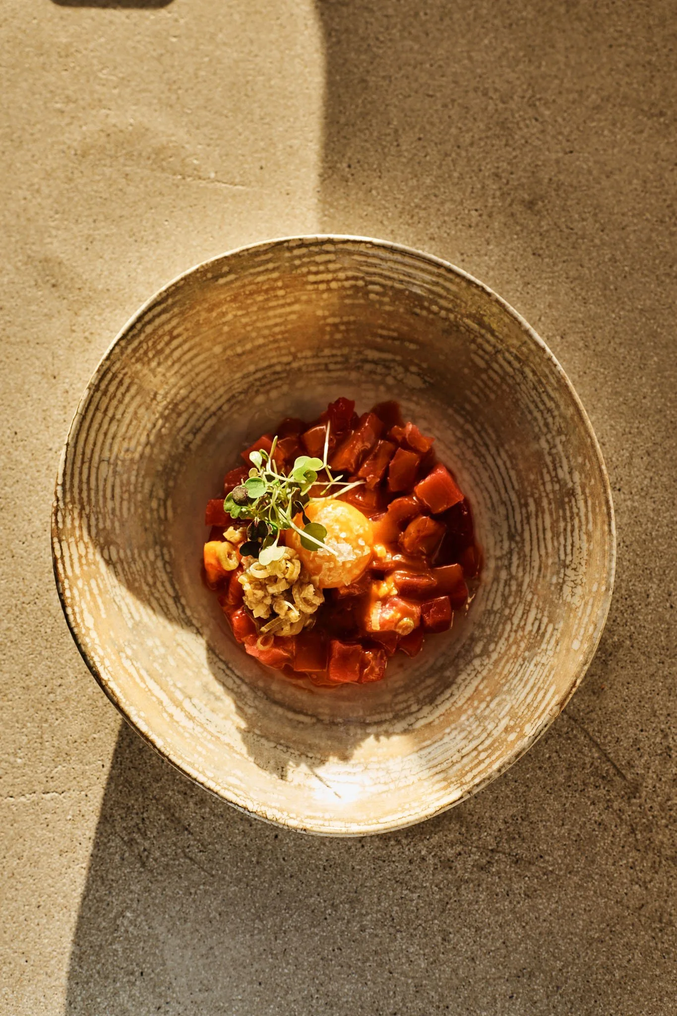 A bowl of diced raw beef tartare topped with microgreens and a raw egg yolk.
