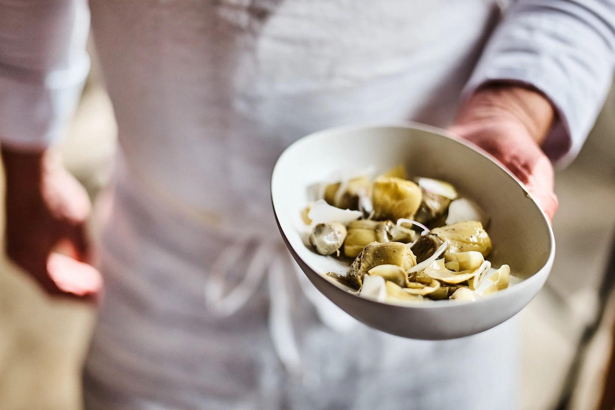 Person holding a bowl of cooked artichoke hearts and garlic cloves