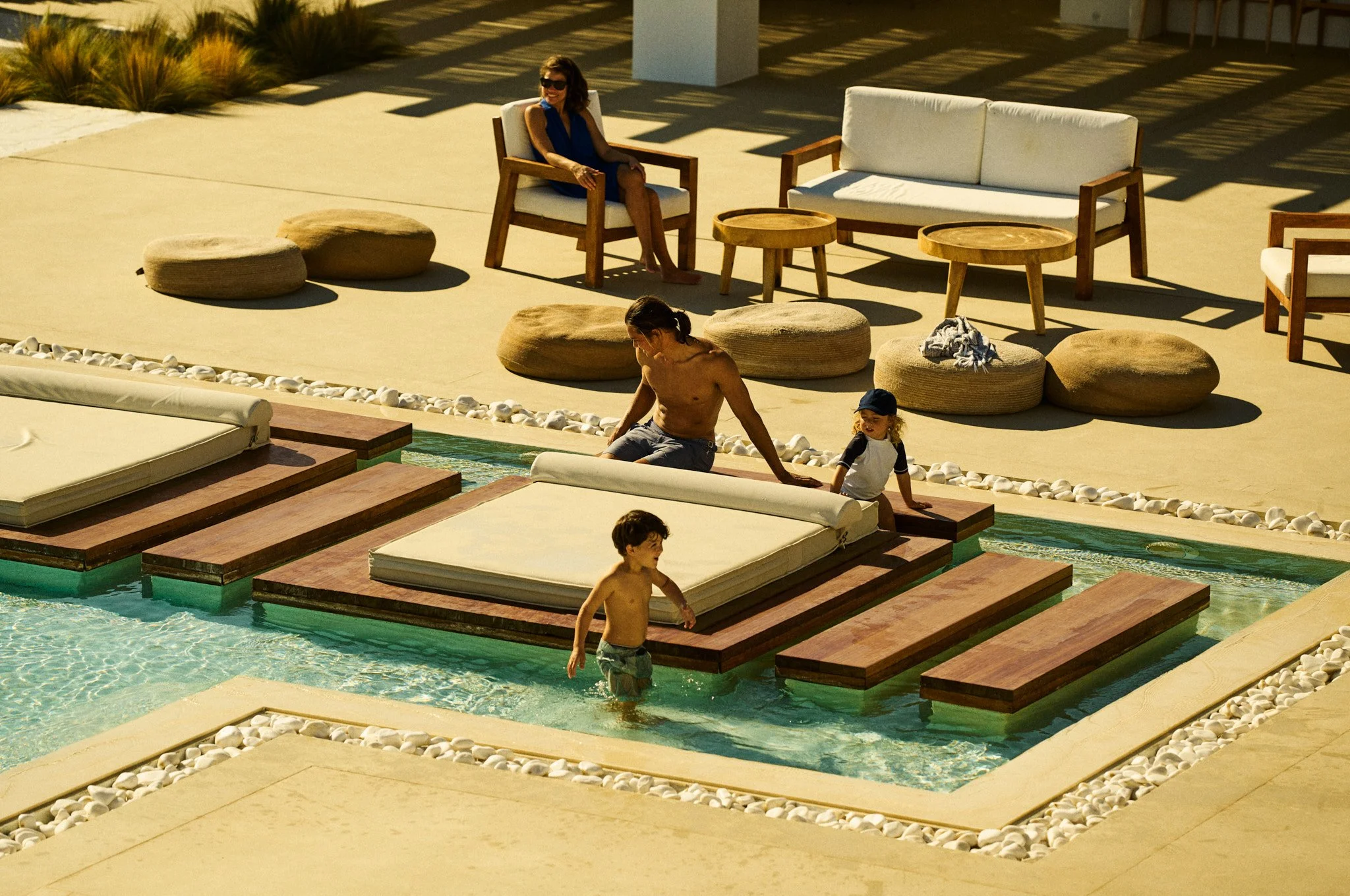A man and children enjoying a poolside area with seating and lounge furniture on a sunny day.