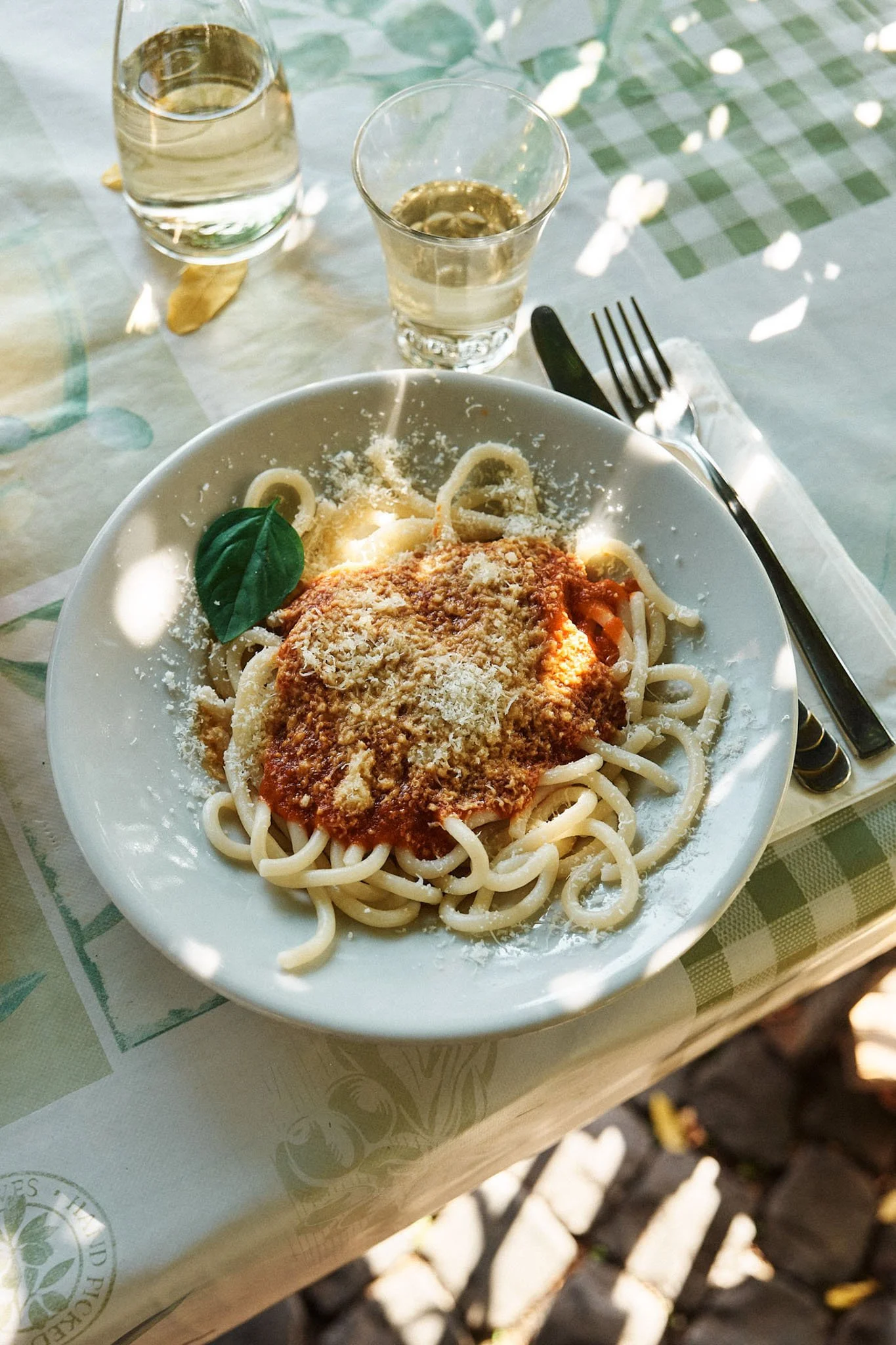 A plate of spaghetti with marinara sauce, grated cheese, and a basil leaf on top, set on a table with two glasses of white wine next to it.