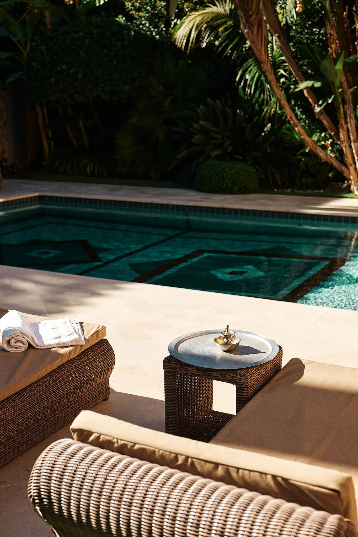View of a backyard with swimming pool, woven outdoor furniture, and lush green tropical plants and trees in the background.