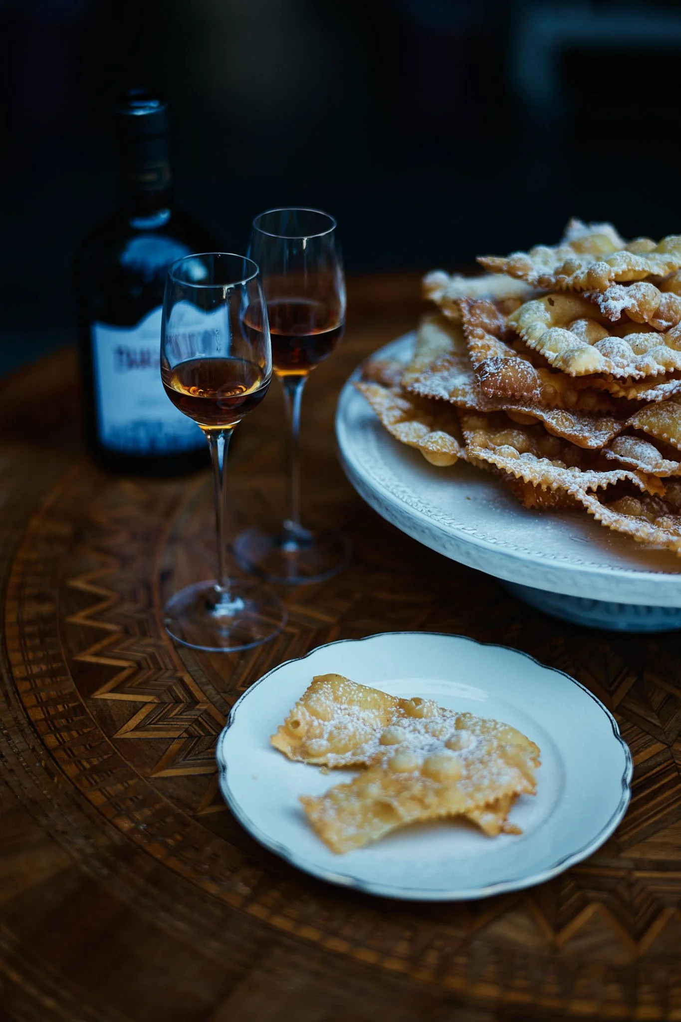 A plate of Italian cannoli with powdered sugar, two glasses of red wine, and a bottle in the background.