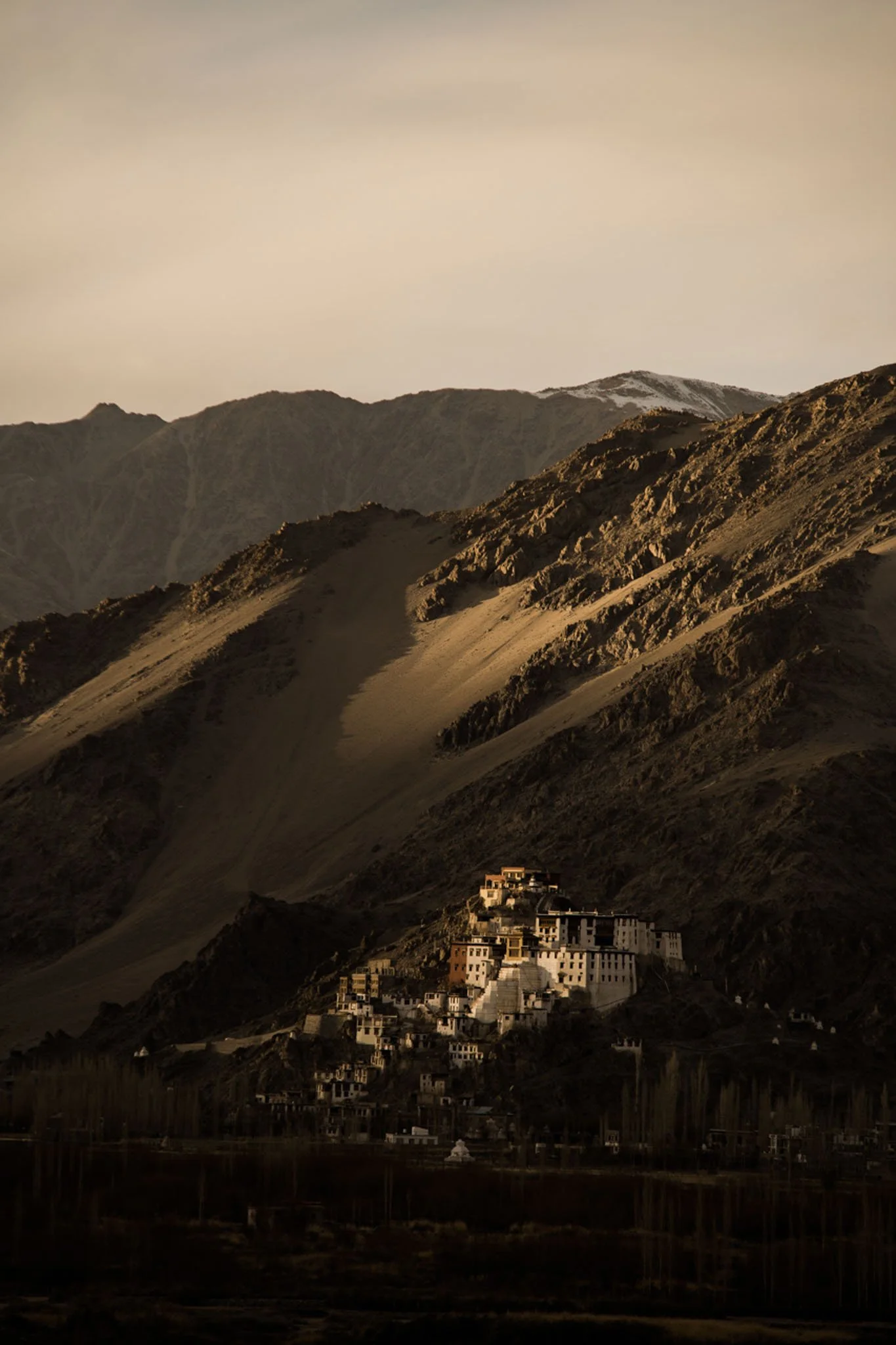 A rugged mountain landscape with a cluster of buildings on the hillside, illuminated by warm sunlight.