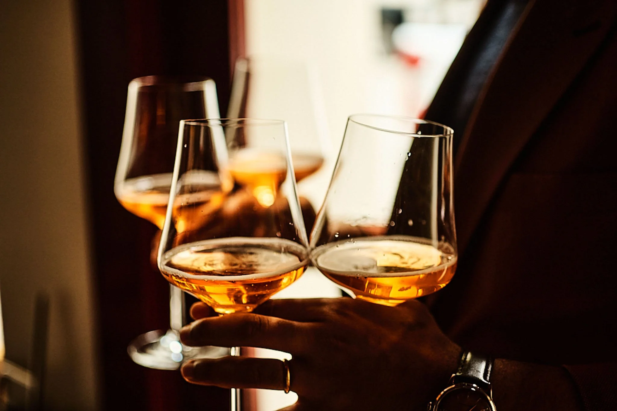 Person holding three glasses of rosé wine in a dimly lit setting.