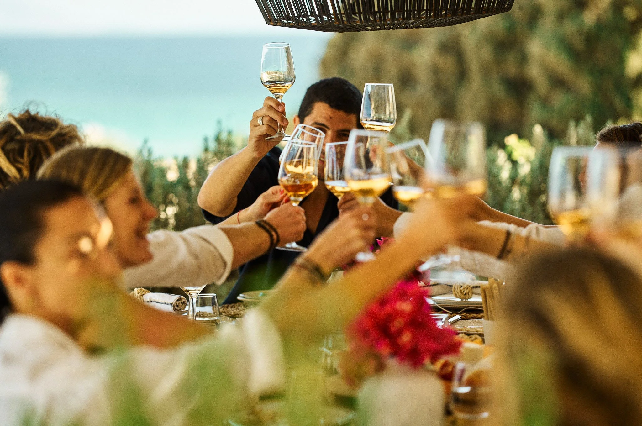 People enjoying a toast with glasses of white wine at an outdoor gathering, with a table set for a celebration.