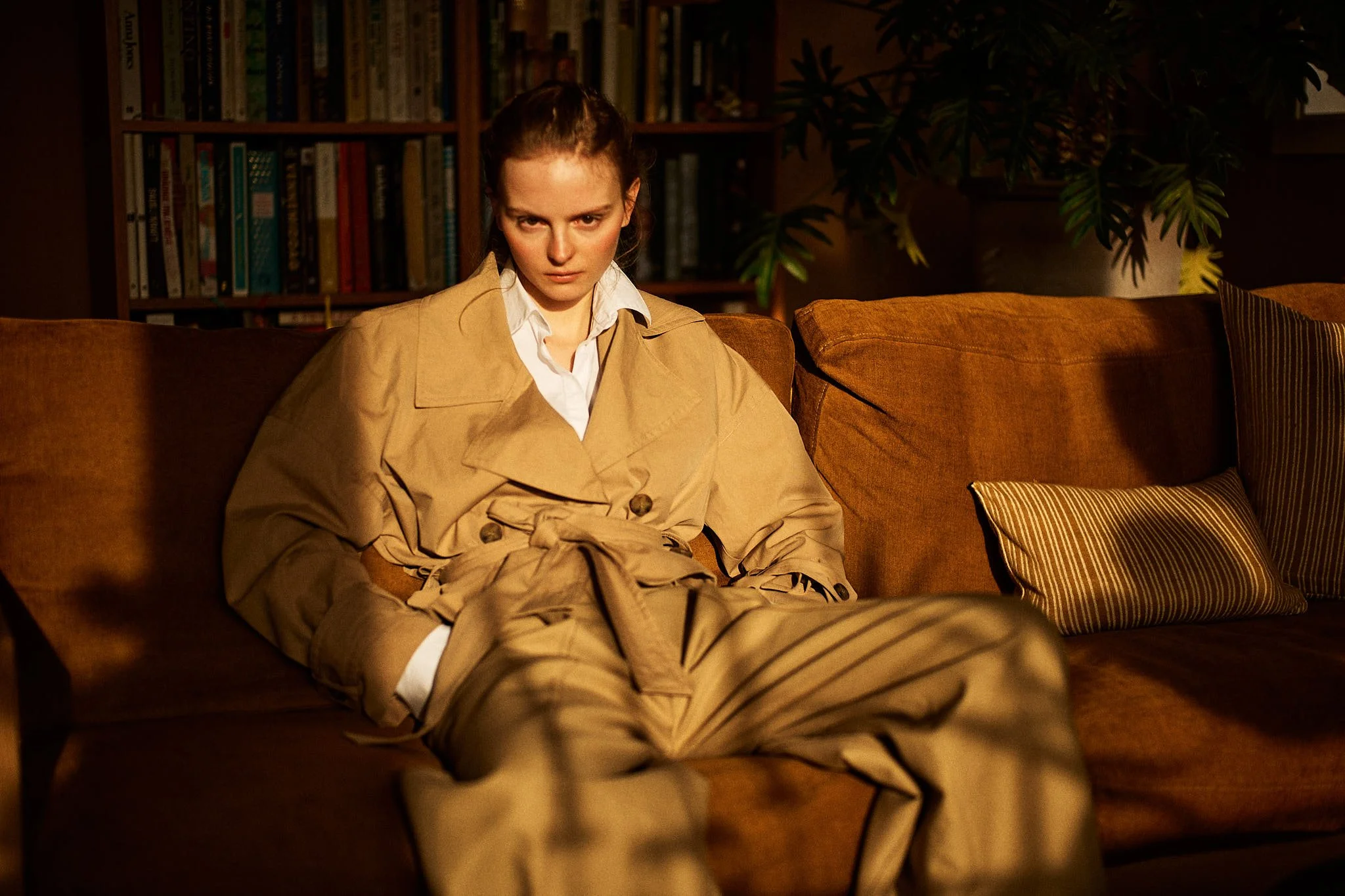Woman in a camel coat on a leather sofa in a library, fashion photography by Oivind Haug