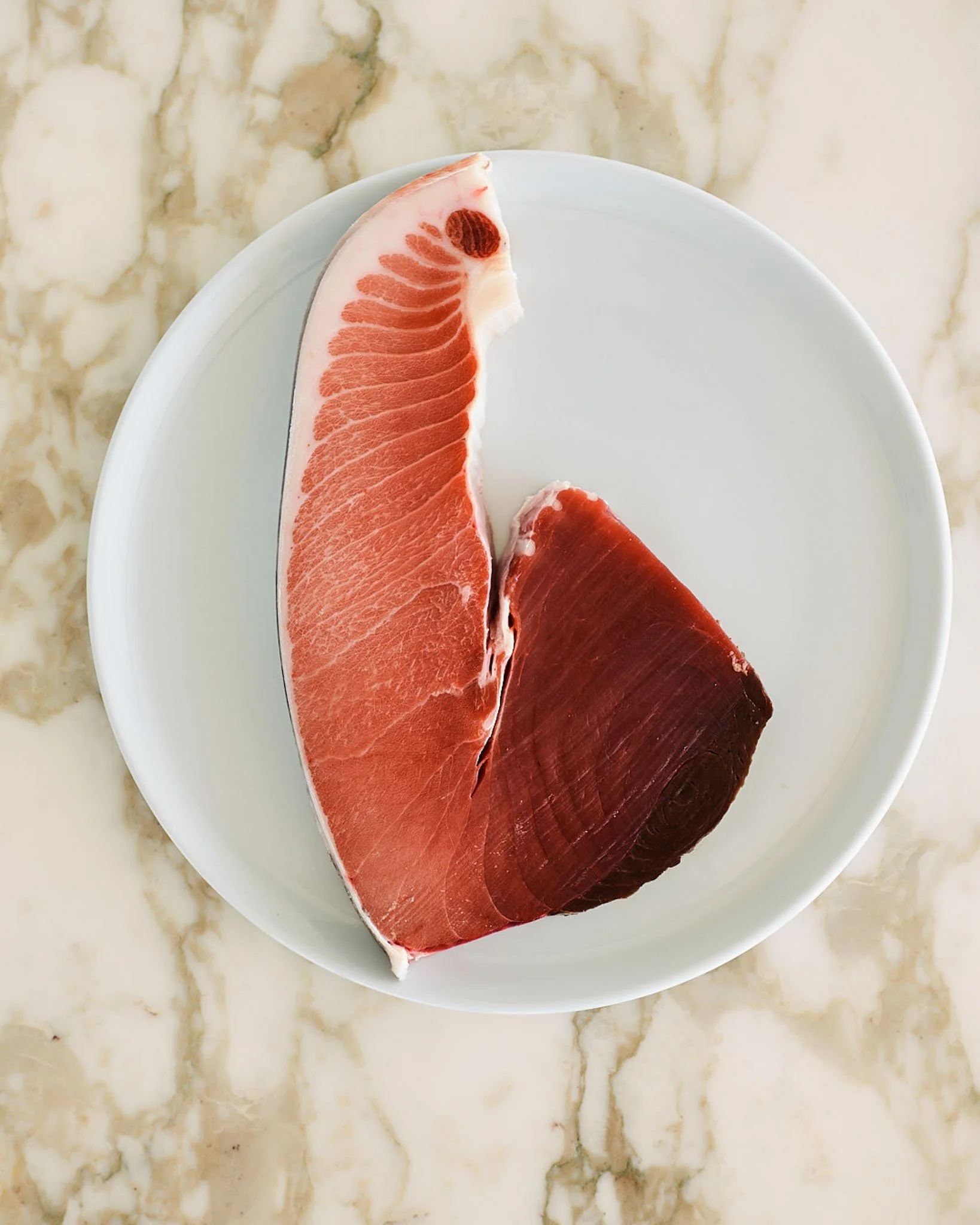 Two pieces of raw fish, one pink and one dark red, on a white plate.