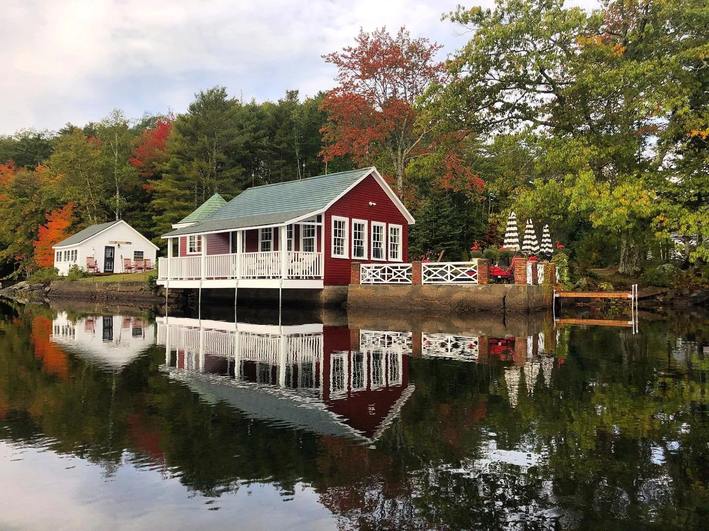 Blenheim Park's Teahouse with white trim and a porch by the water, surrounded by trees with autumn foliage, reflected in the calm water.