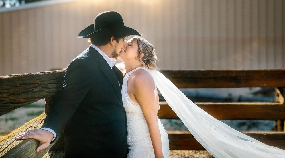 A couple kissing at sunset beside a rustic wooden fence