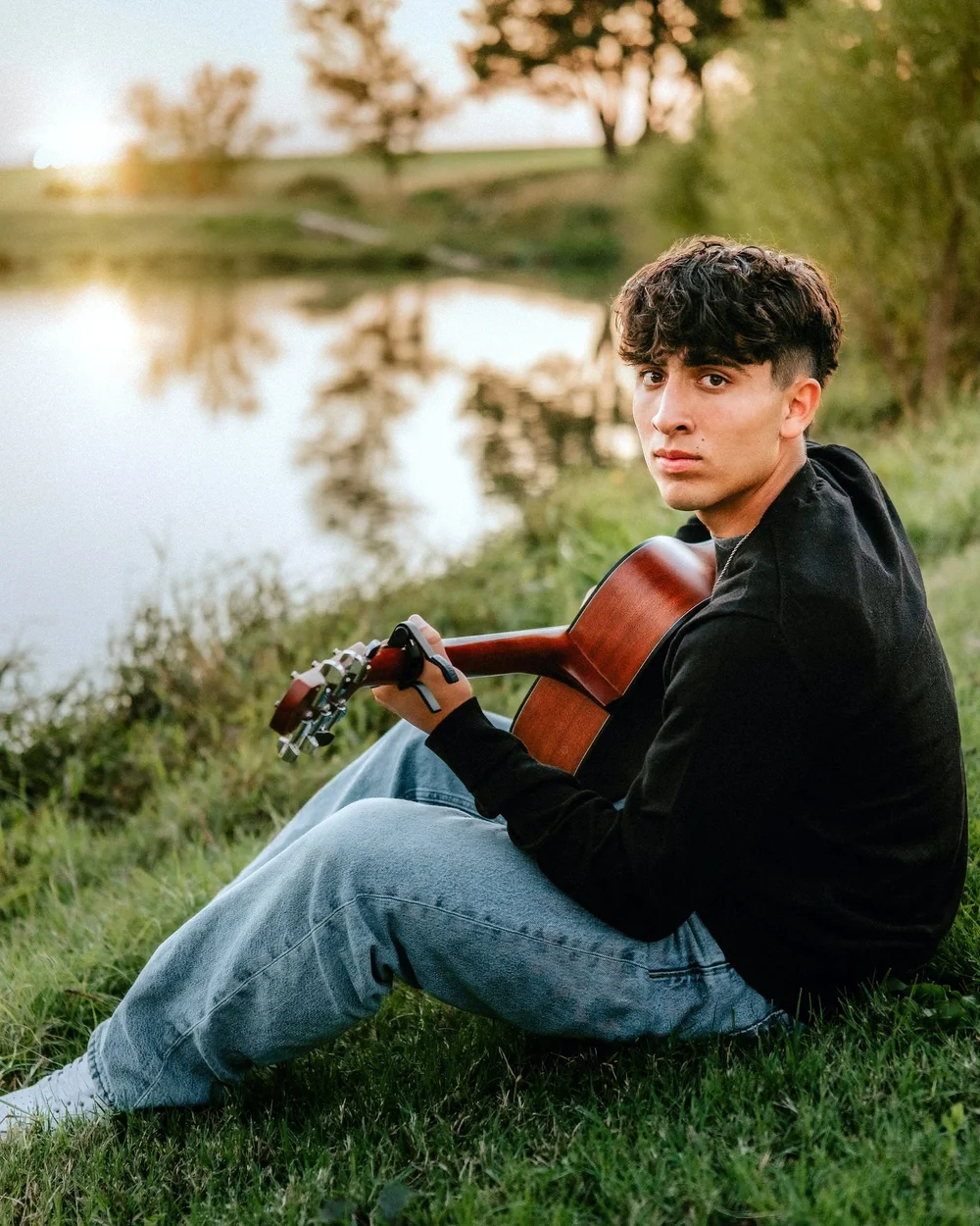 Senior boy by the water at sunset holding a guitar