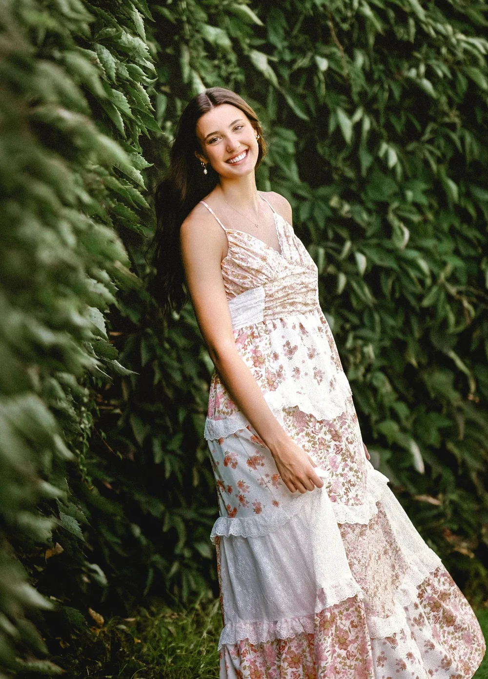 Senior girl in a floral dress beside green plants
