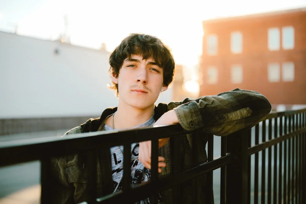 Senior leaning on a black metal fence at sunset