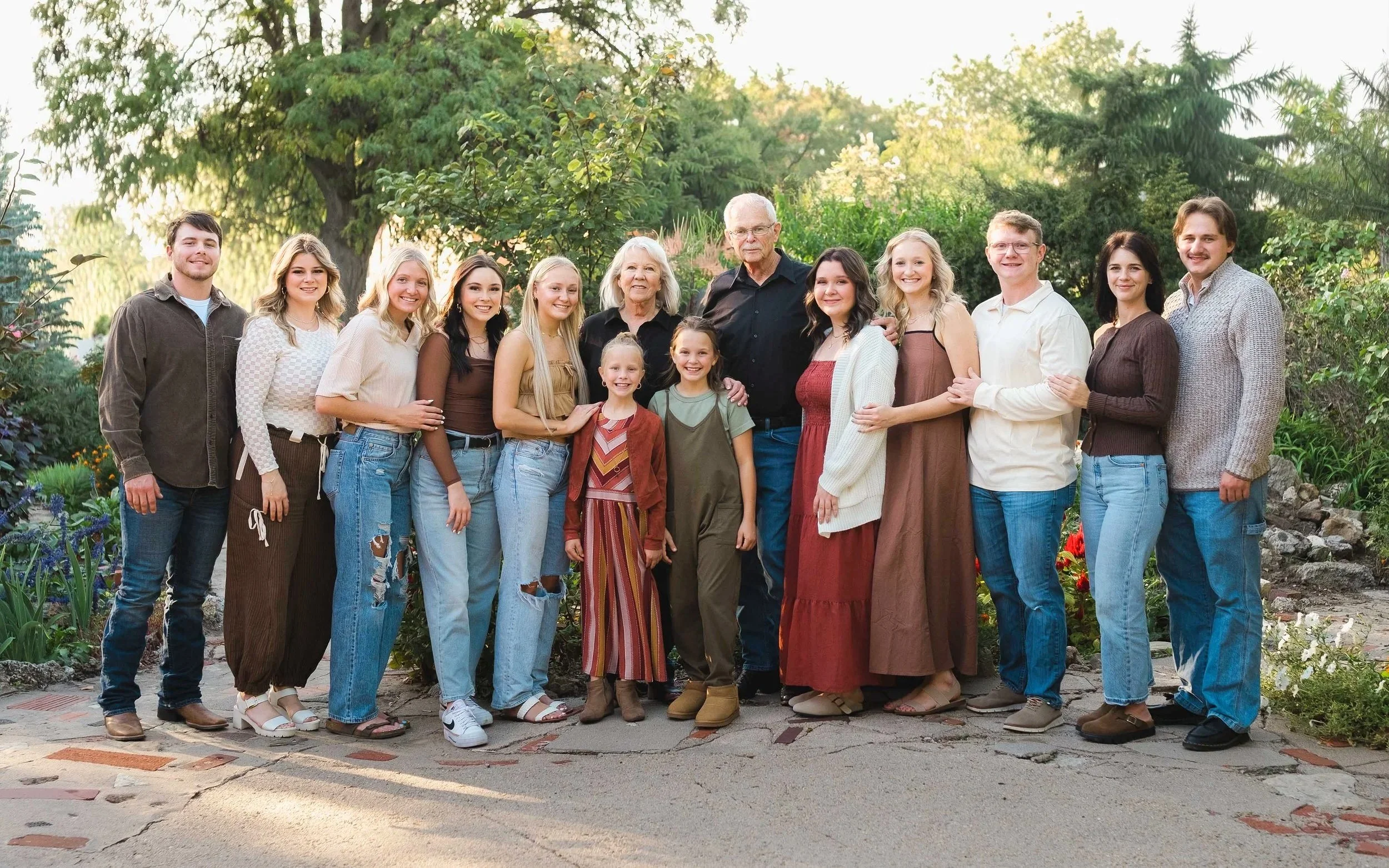 A large family group standing outdoors in a garden, with trees and bushes in the background. The family members are smiling and standing closely together.