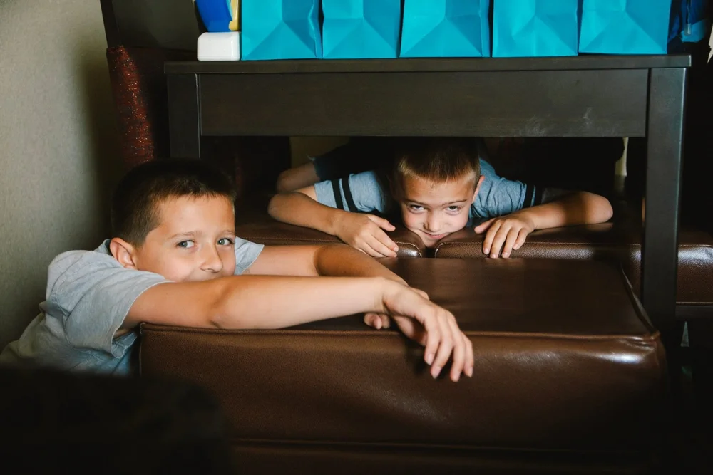 Two young boys playing hide and seek under a table
