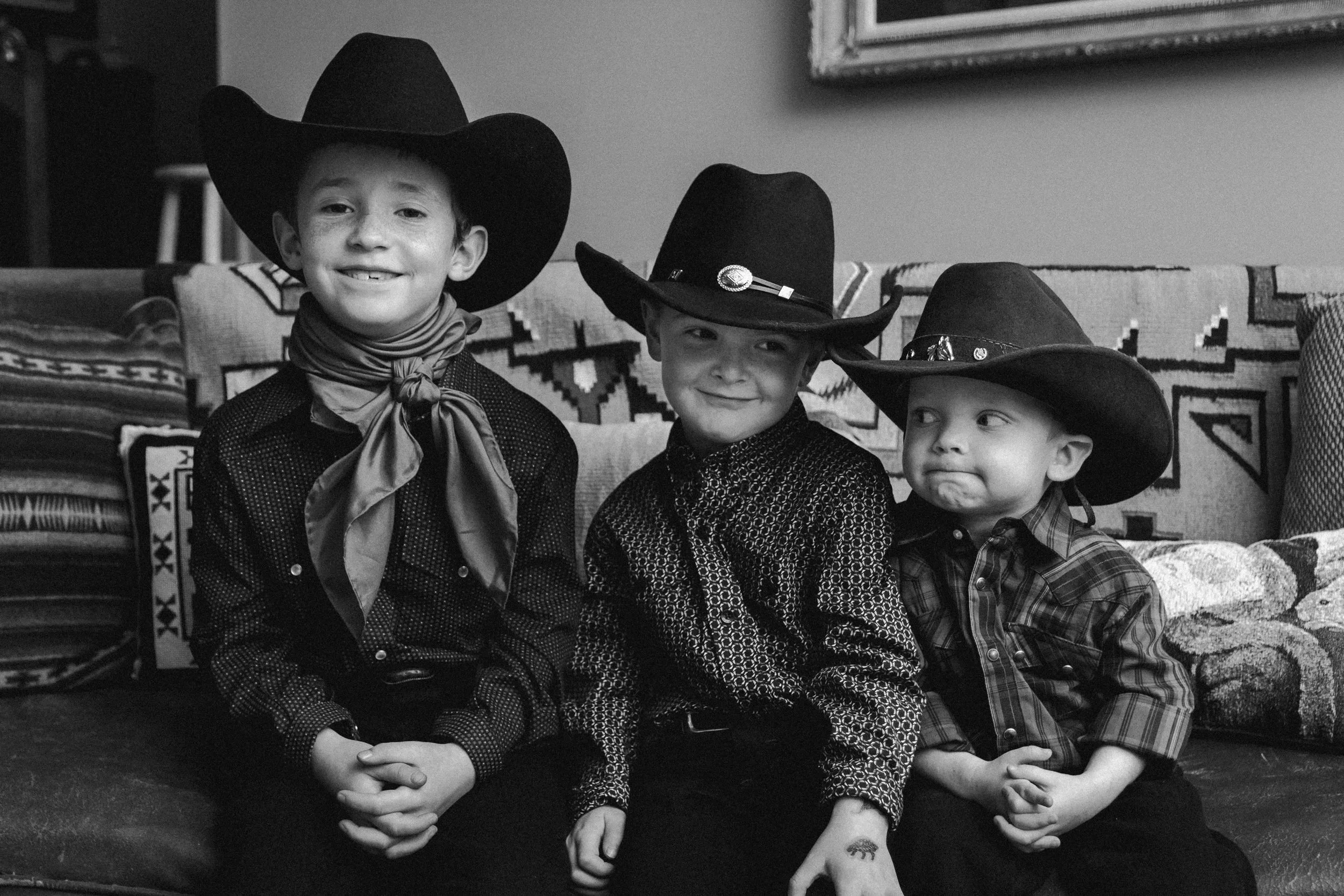 Three young boys dressed as cowboys sitting on a couch in costumes with hats and bandanas.