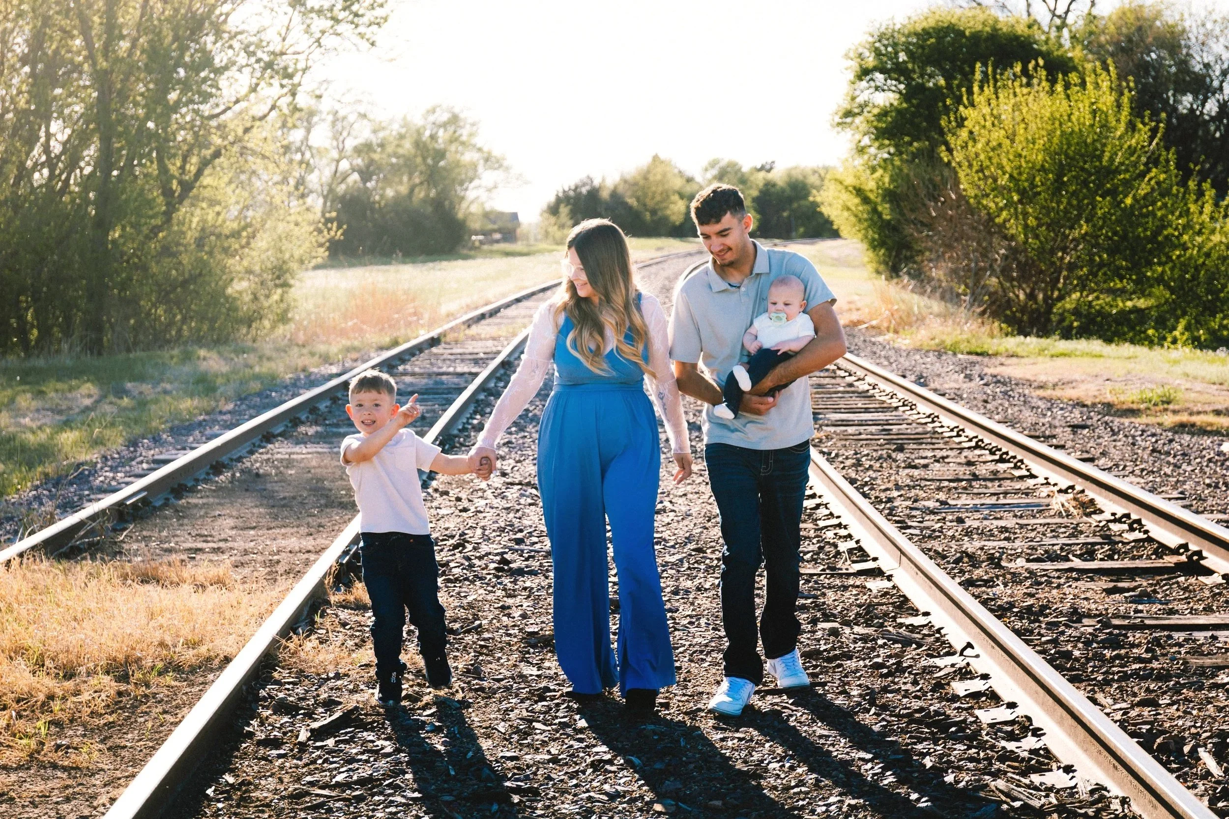 A family of four walking hand in hand on train tracks at sunset in Great Bend, Kansas