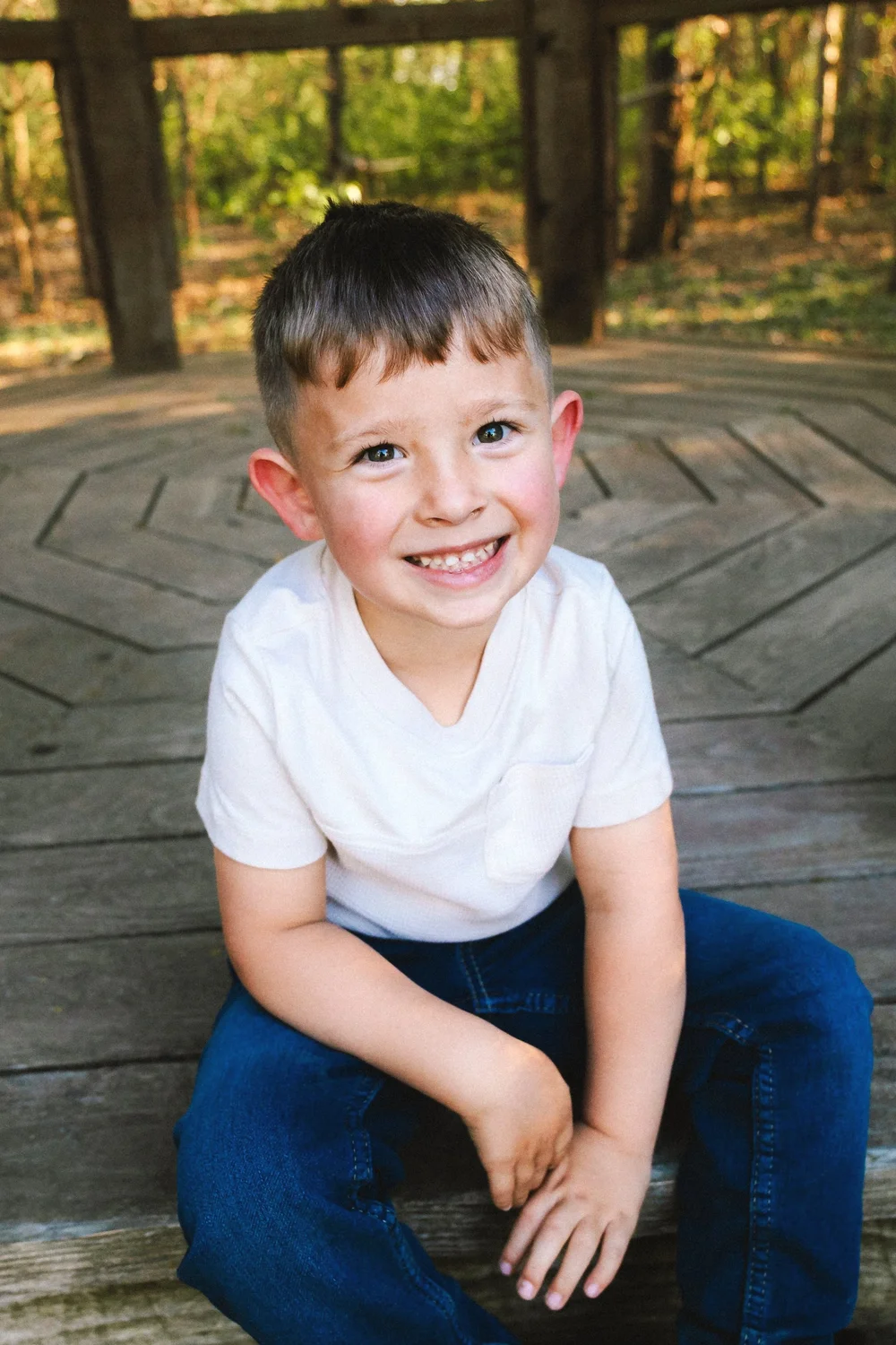 A smiling young boy sitting on a wooden platform outdoors