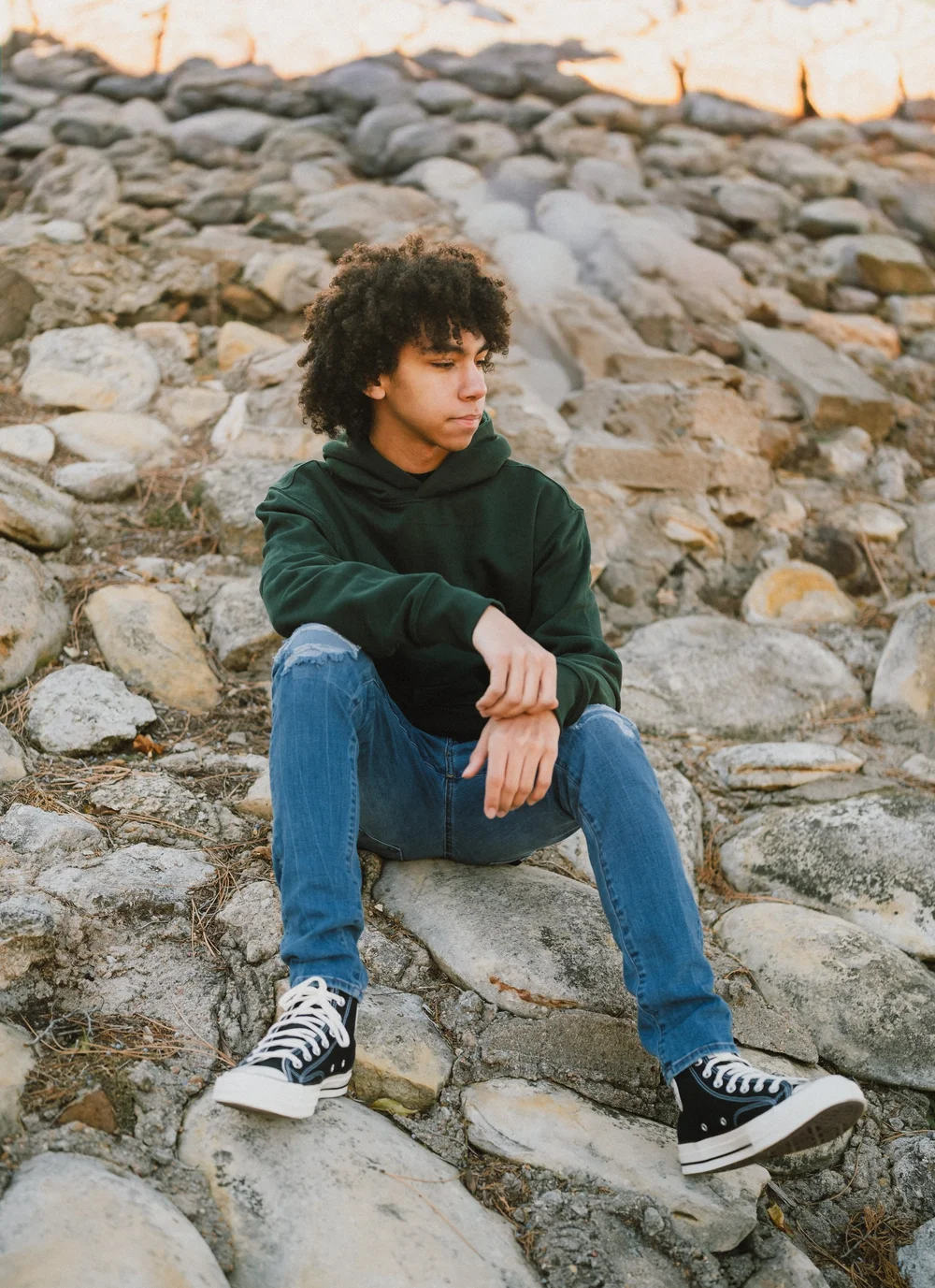 Senior sitting on rocks near the water in a green hoodie