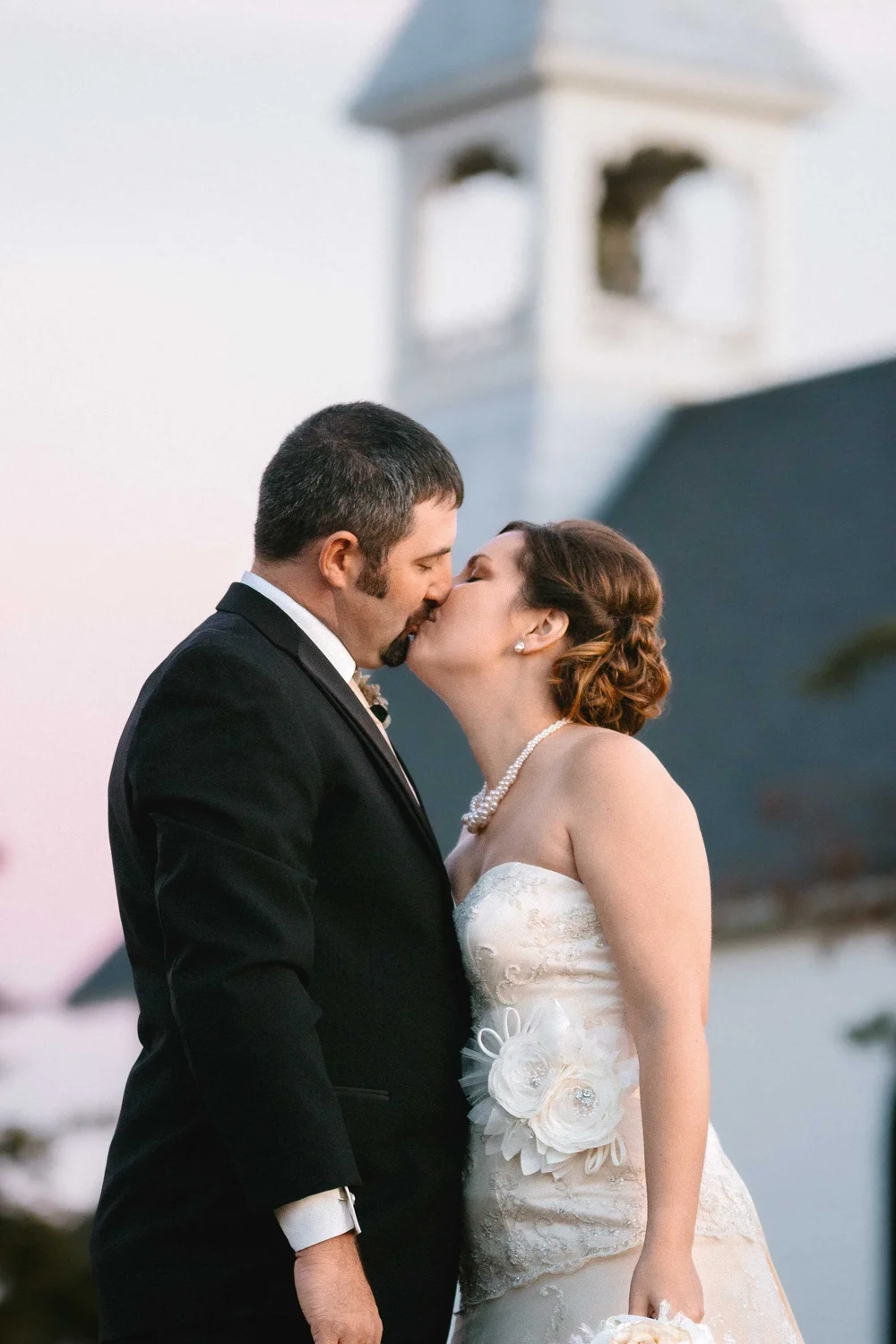 Bride and groom kissing with a church steeple behind them