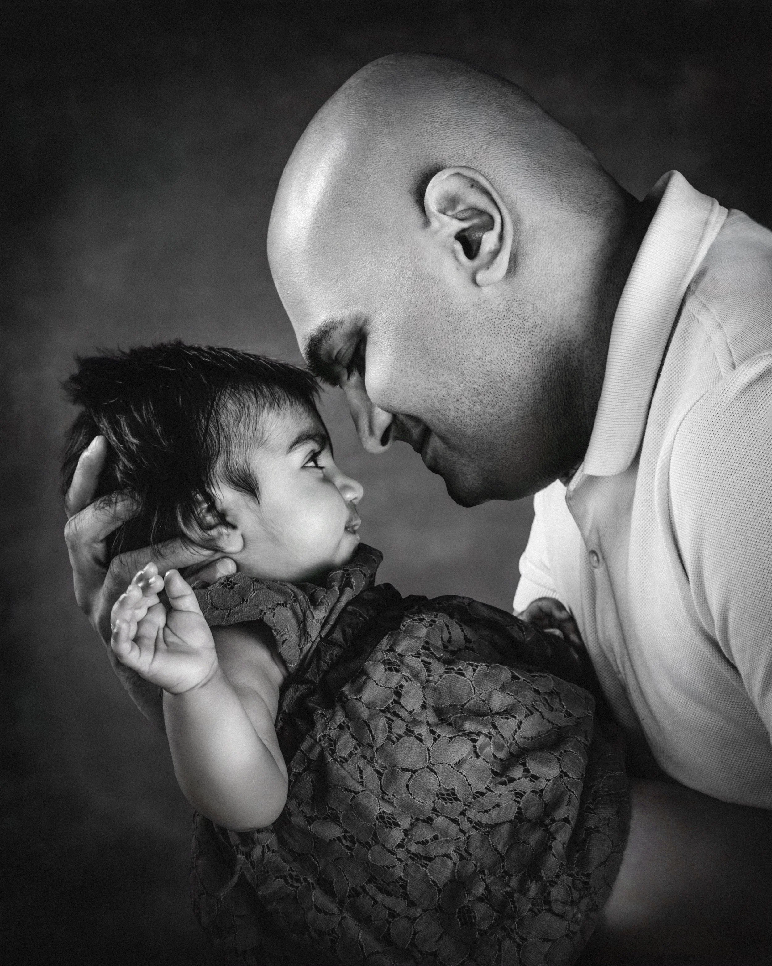A black and white photo of a man and a young child touching foreheads and looking into each other's eyes, with the man smiling gently.